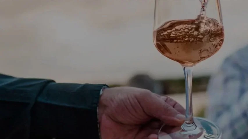 A hand holding a glass of rosé wine outdoors, with a blurred background.