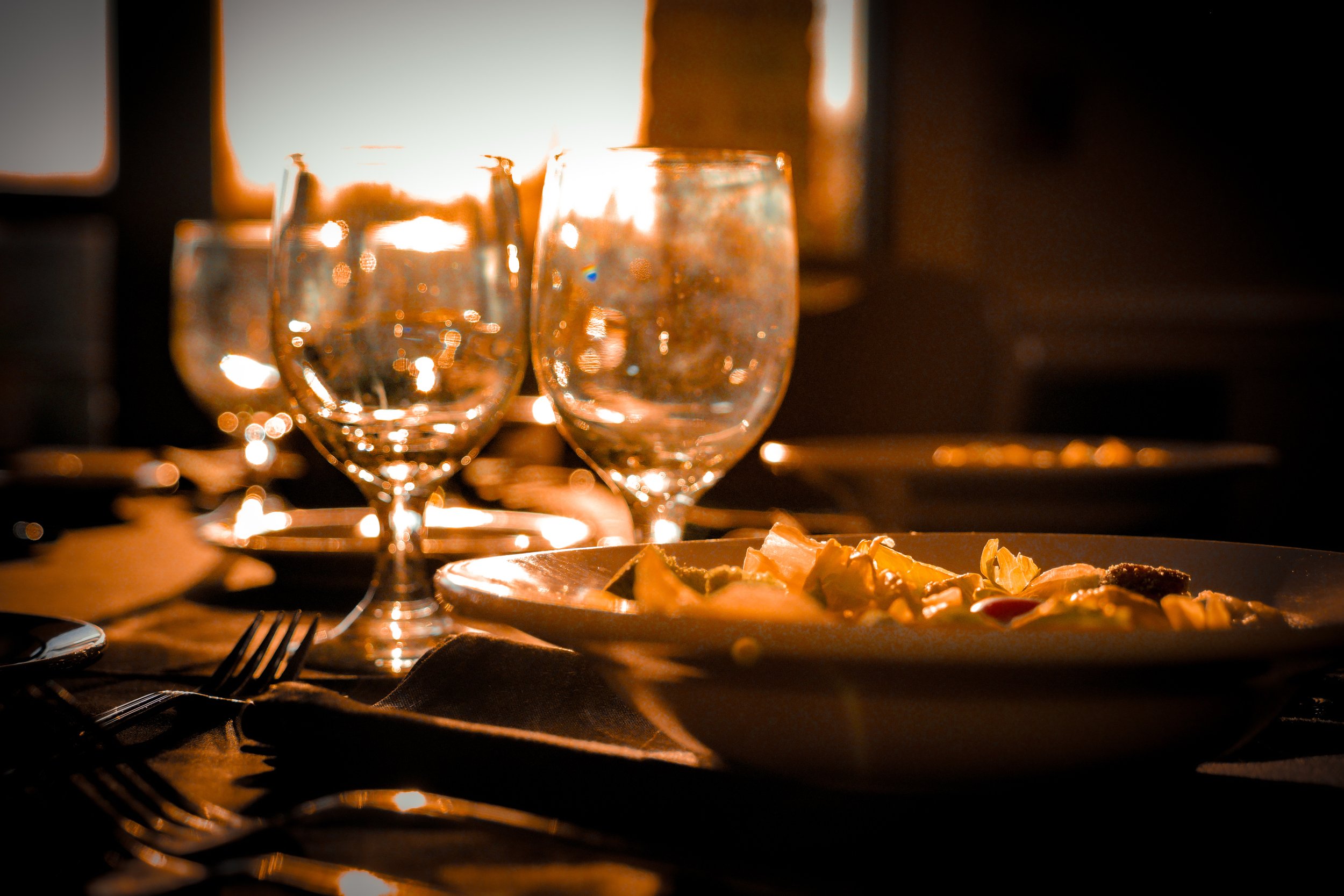 Empty wine glasses on a dimly lit table with a plate of food, possibly at a restaurant or dinner setting.