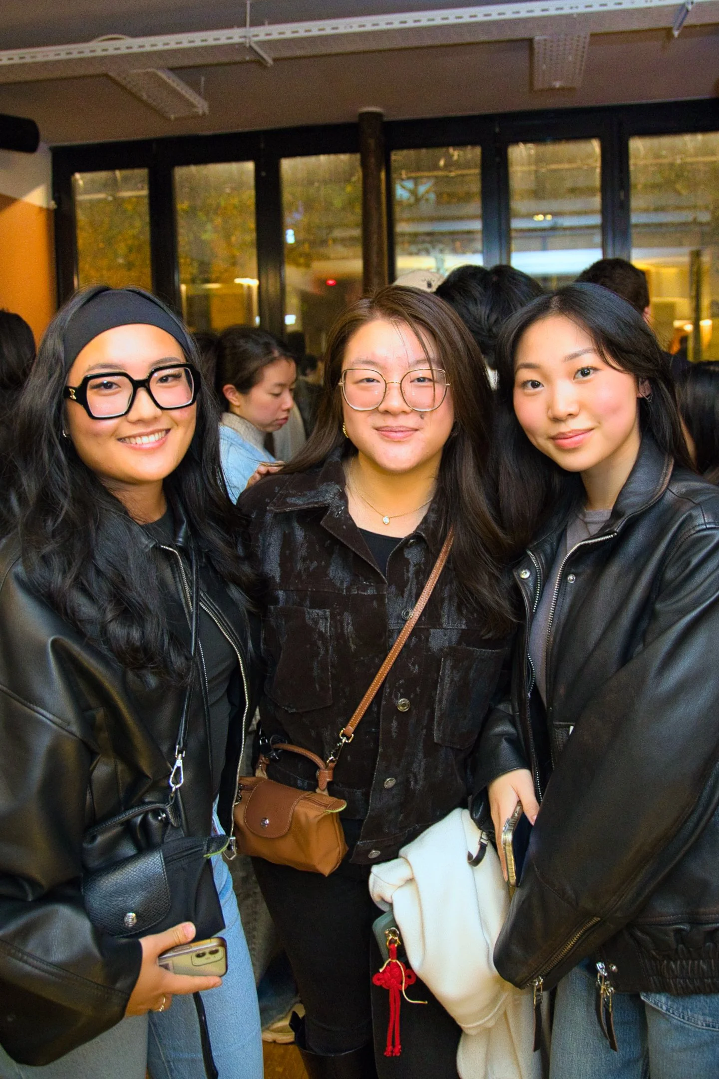 Trois jeunes femmes souriantes et habillées en noir posent pour une photo dans une ambiance sociale en intérieur. soirée networking AJCF