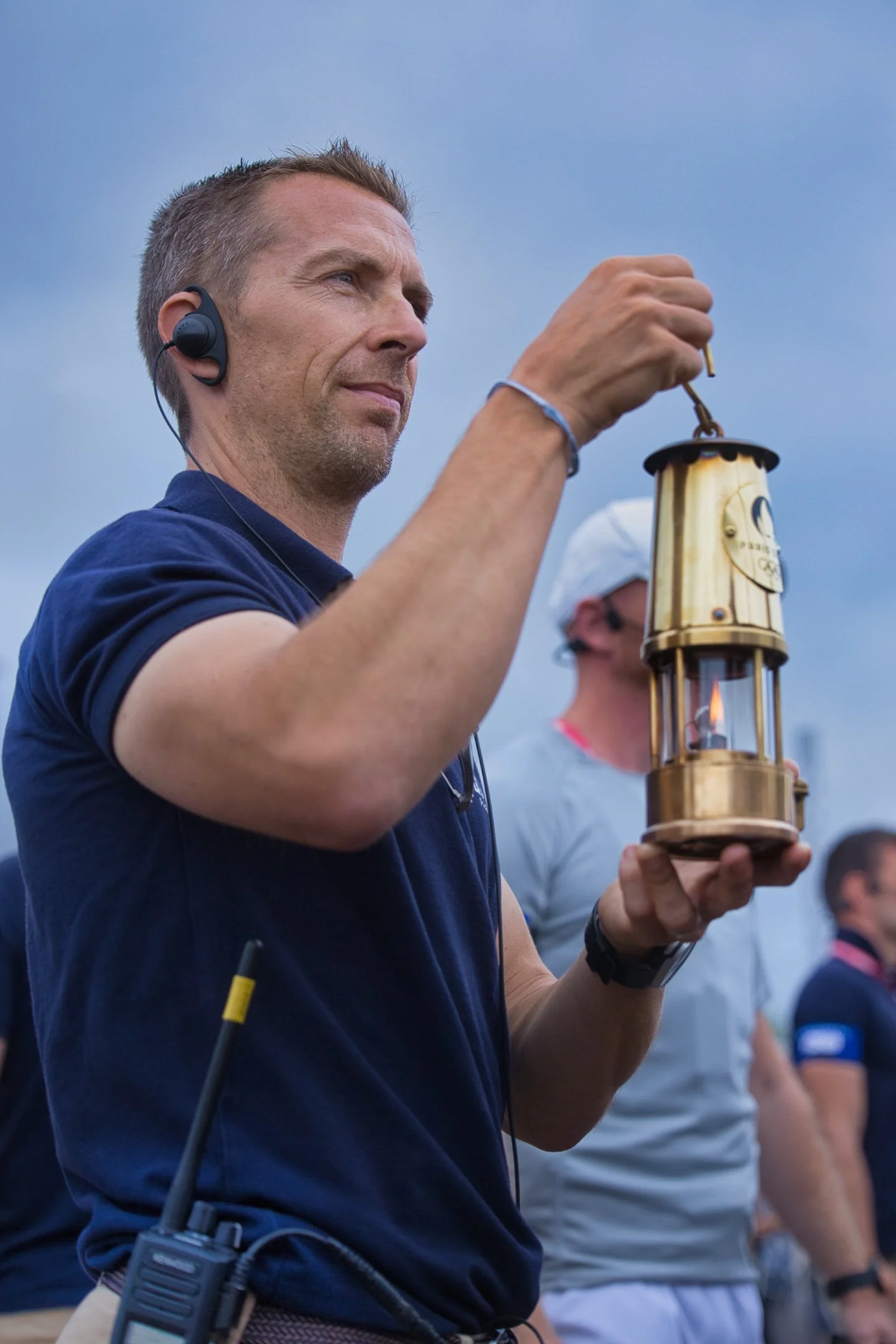 Homme tenant une lanterne en métal lors d'une cérémonie JO Paris 2024.