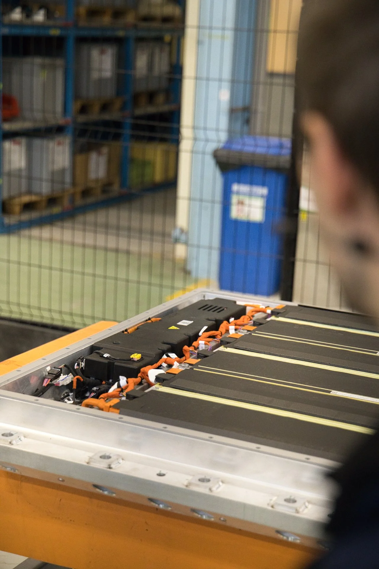 Une personne observe une batterie de véhicule électrique avec des câbles orange sur une table, dans un environnement industriel ou de stockage. Ampere groupe Renault