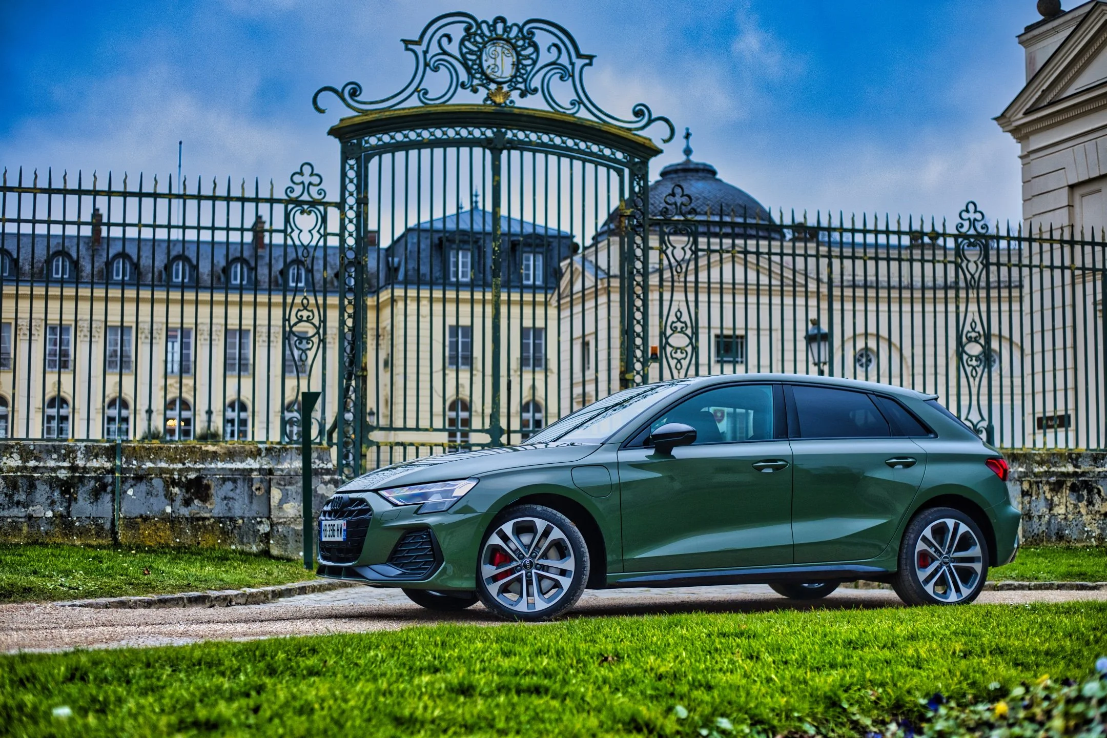 Audi A3 45 TFSIe verte stationnée devant une grille en fer forgé et un bâtiment résidentiel en arrière-plan.