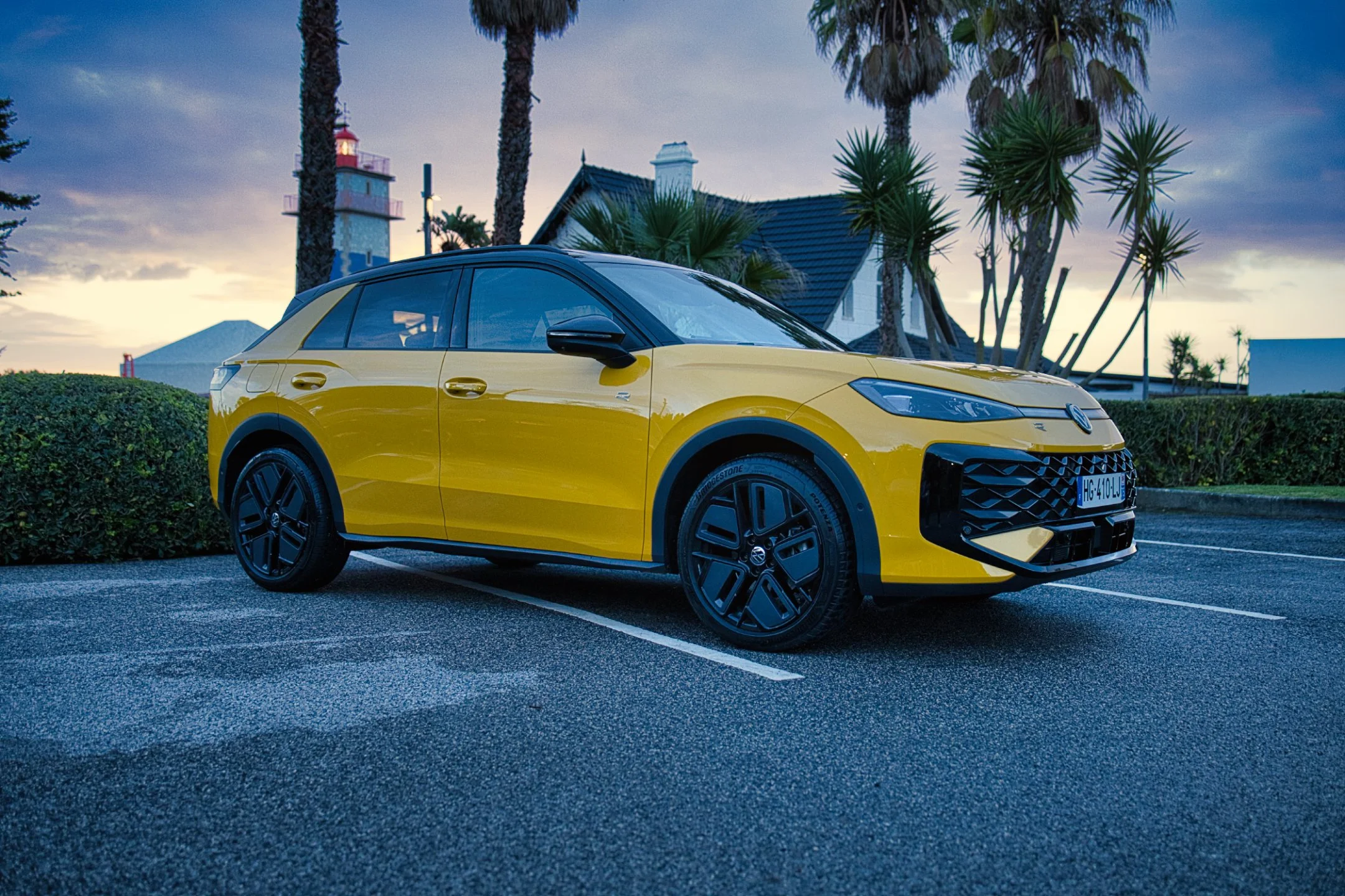Nouvelle VW T-Roc jaune garée dans un parking avec des palmiers et une maison en arrière-plan, ciel au levé du jour au Portugal Caiscais