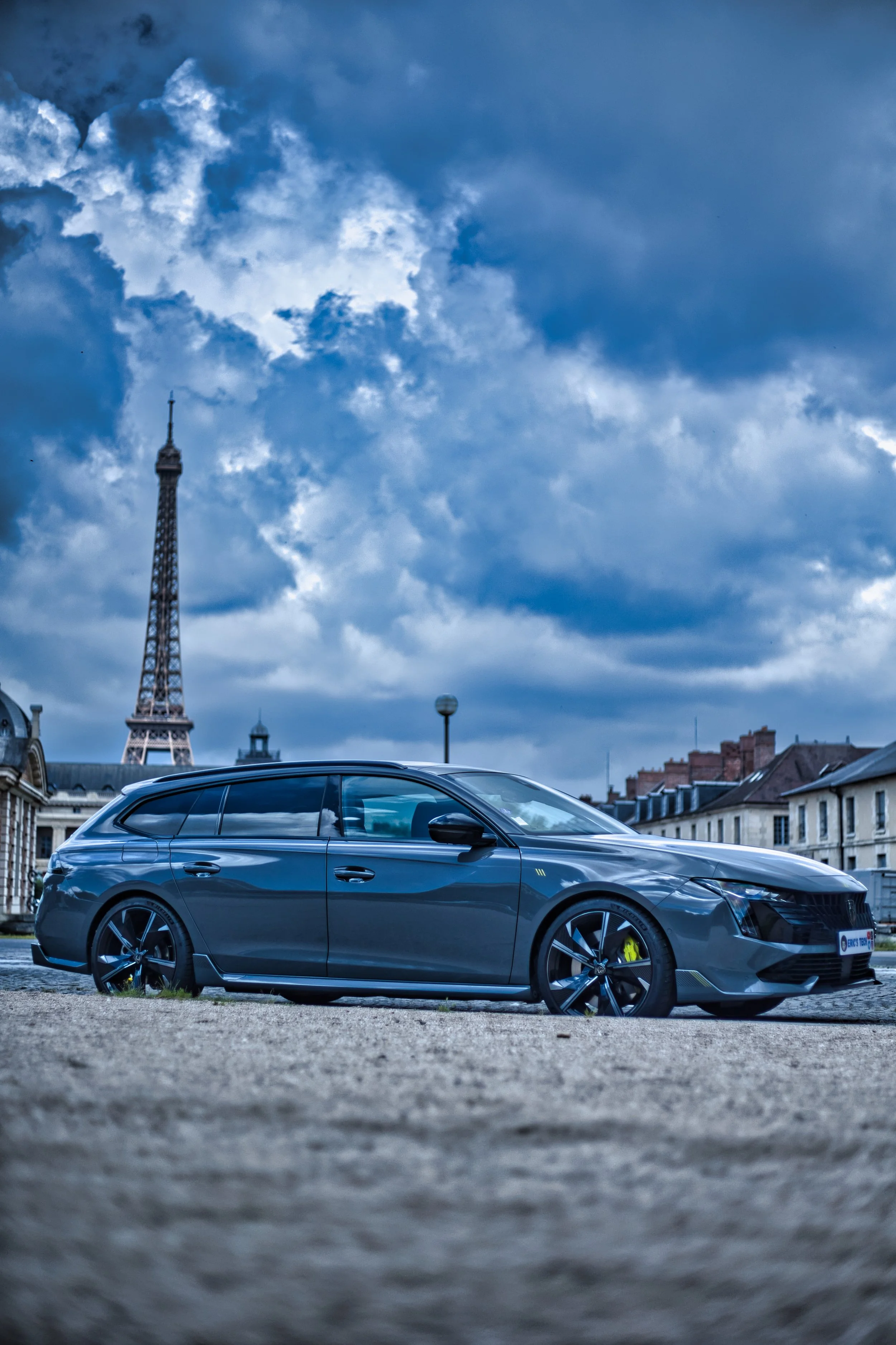 Voiture grise stationnée sur une place avec la Tour Eiffel en arrière-plan, sous un ciel nuageux à Paris. Peugeot 508 SW PSE