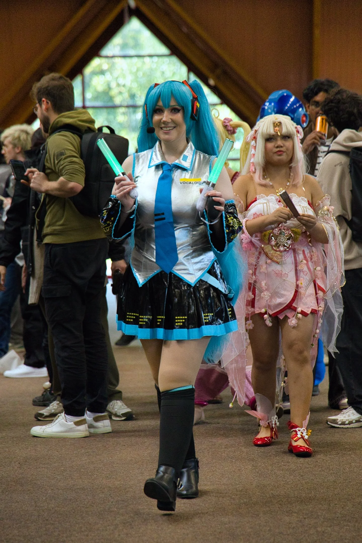 Deux femmes déguisées en personnages d'anime ou de jeux vidéo, l'une en costume bleu avec des lumières LED et une perruque bleue, l'autre en costume rose avec des accessoires floraux, lors l'évènement Gaming Théodasium à Thiais