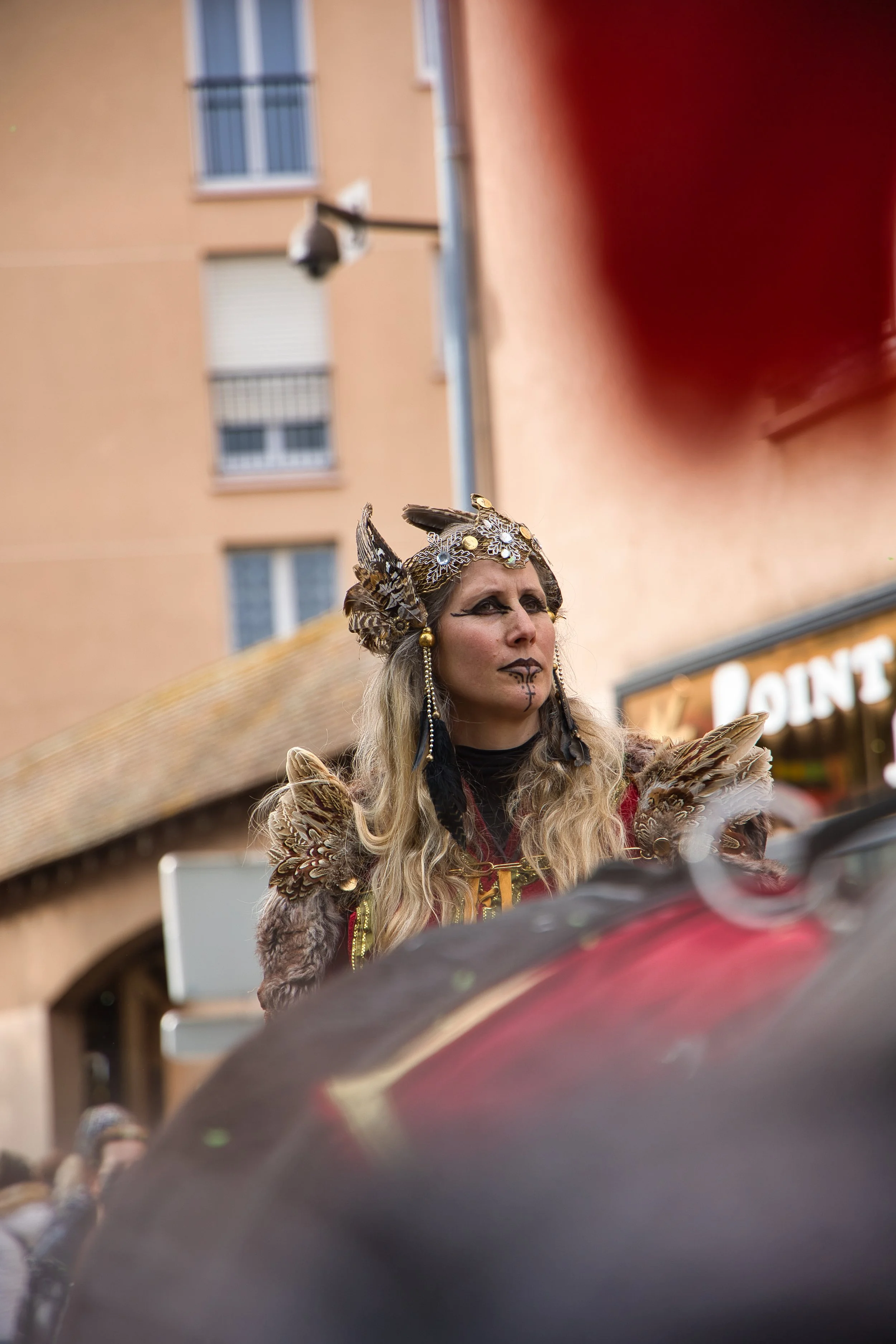 Femme déguisée en costume de sorcière ou de créature mythologique, avec un maquillage sombre et des accessoires ornés de plumes et de bijoux, lors du carnaval de Thiais