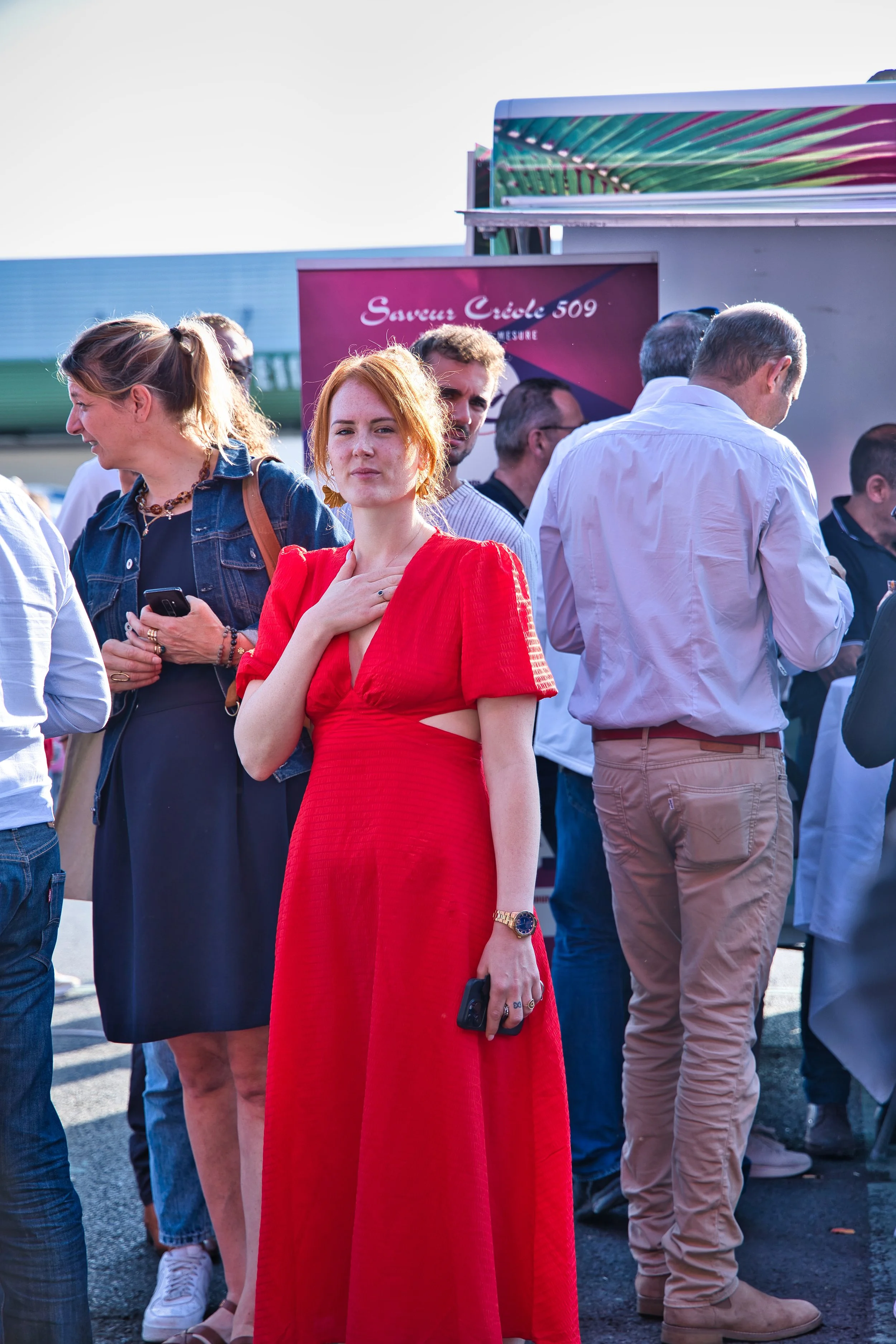 Une femme en robe rouge pose pour la photo lors d'un événement en plein air, entourée par d'autres personnes fête de la musique au marché de Rungis