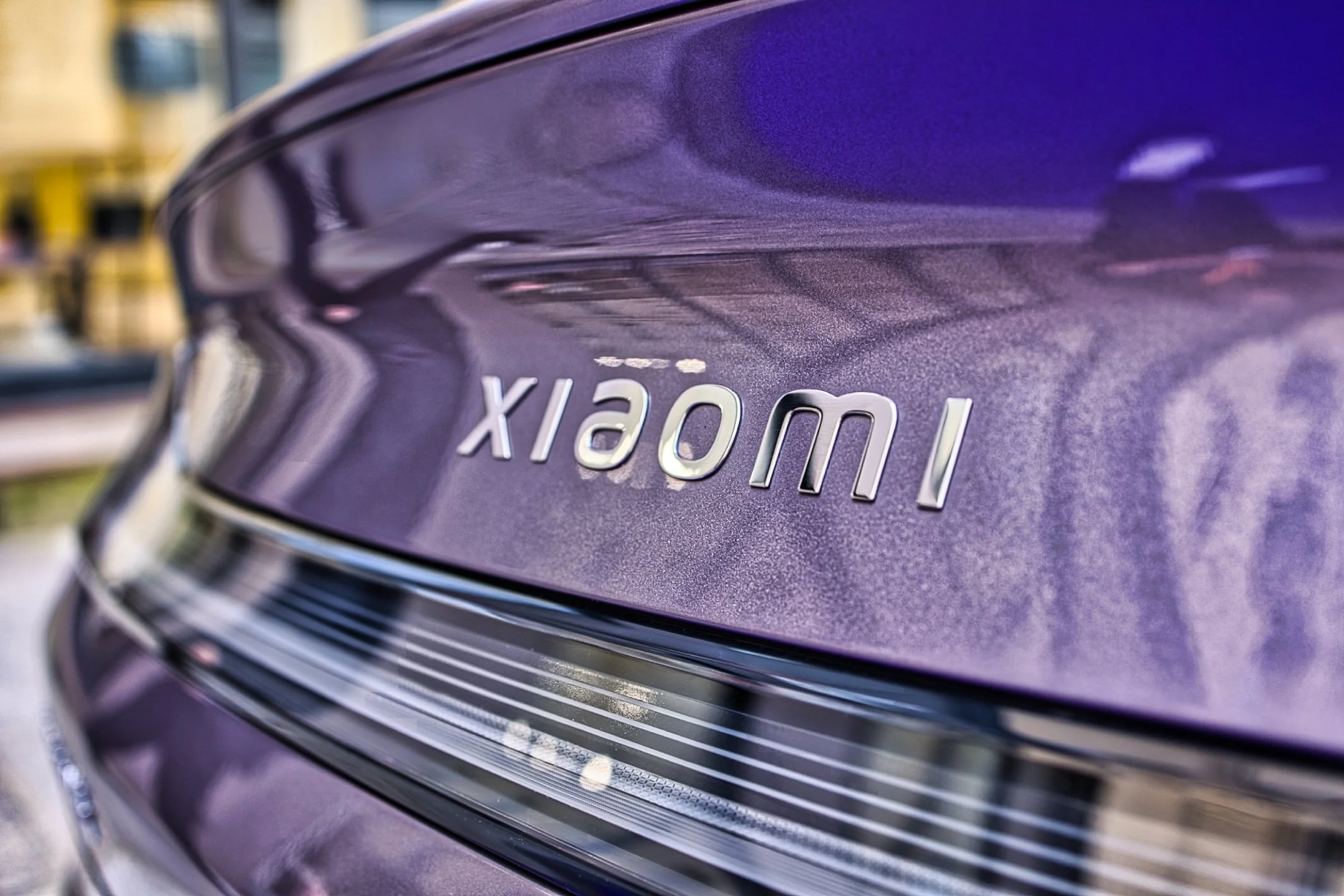 Une voiture violette avec le logo 'Xiaomi' sur le coffre. Il s'agit probablement d'une voiture électrique ou d'un concept. L'image est prise en extérieur avec un reflet sur la carrosserie. Xiaomi SU7 Max