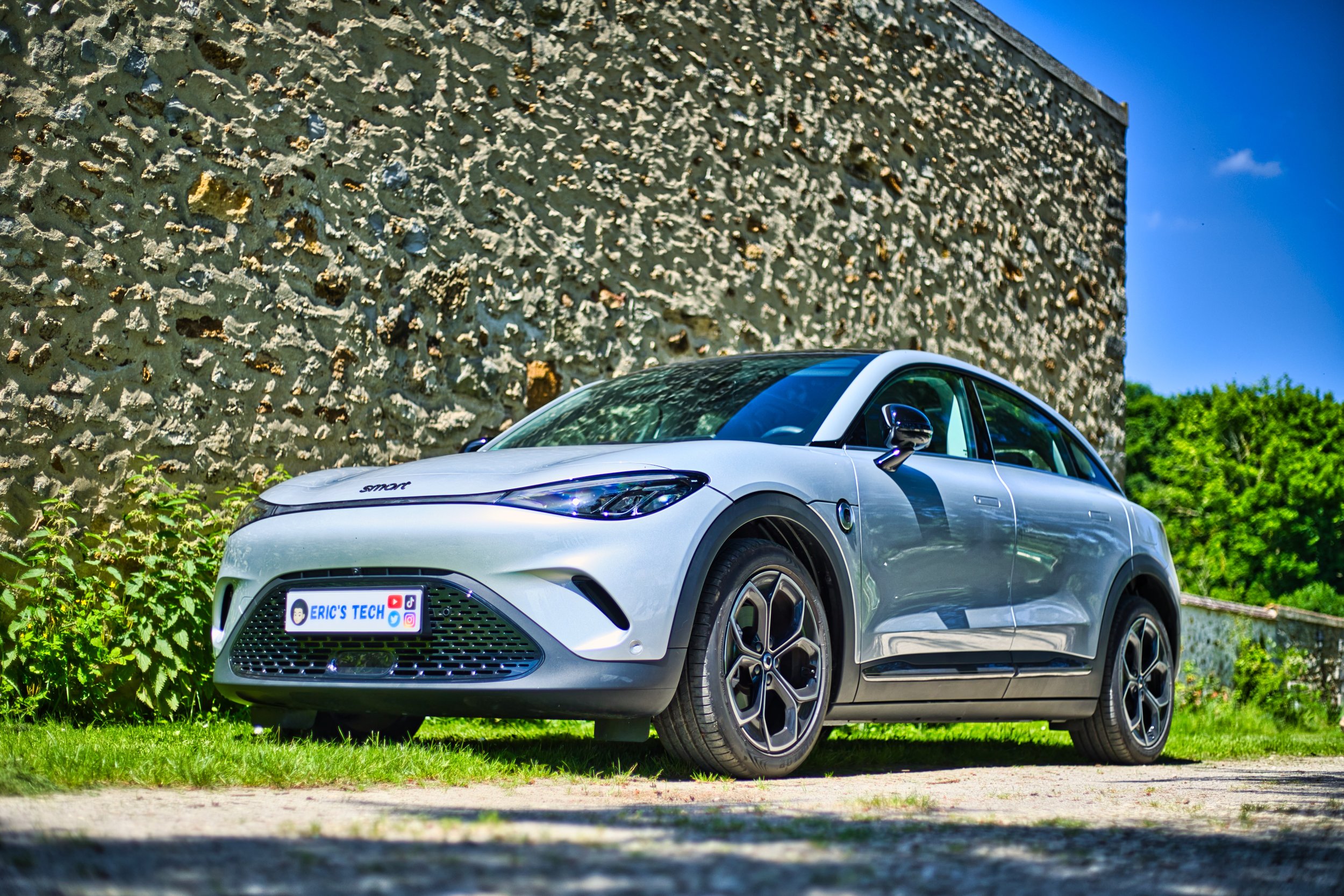 Smart #3, stationnée en extérieur près d'un mur en pierre, sous un ciel bleu.