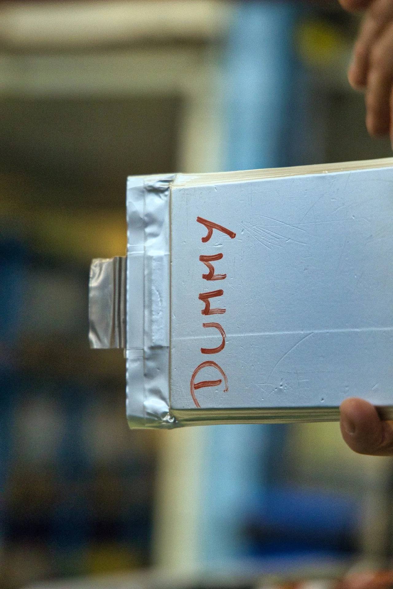 Une personne tient un cellule de batterie factice 'Dummy' écrit dessus en rouge manuscrit. Ampere groupe Renault