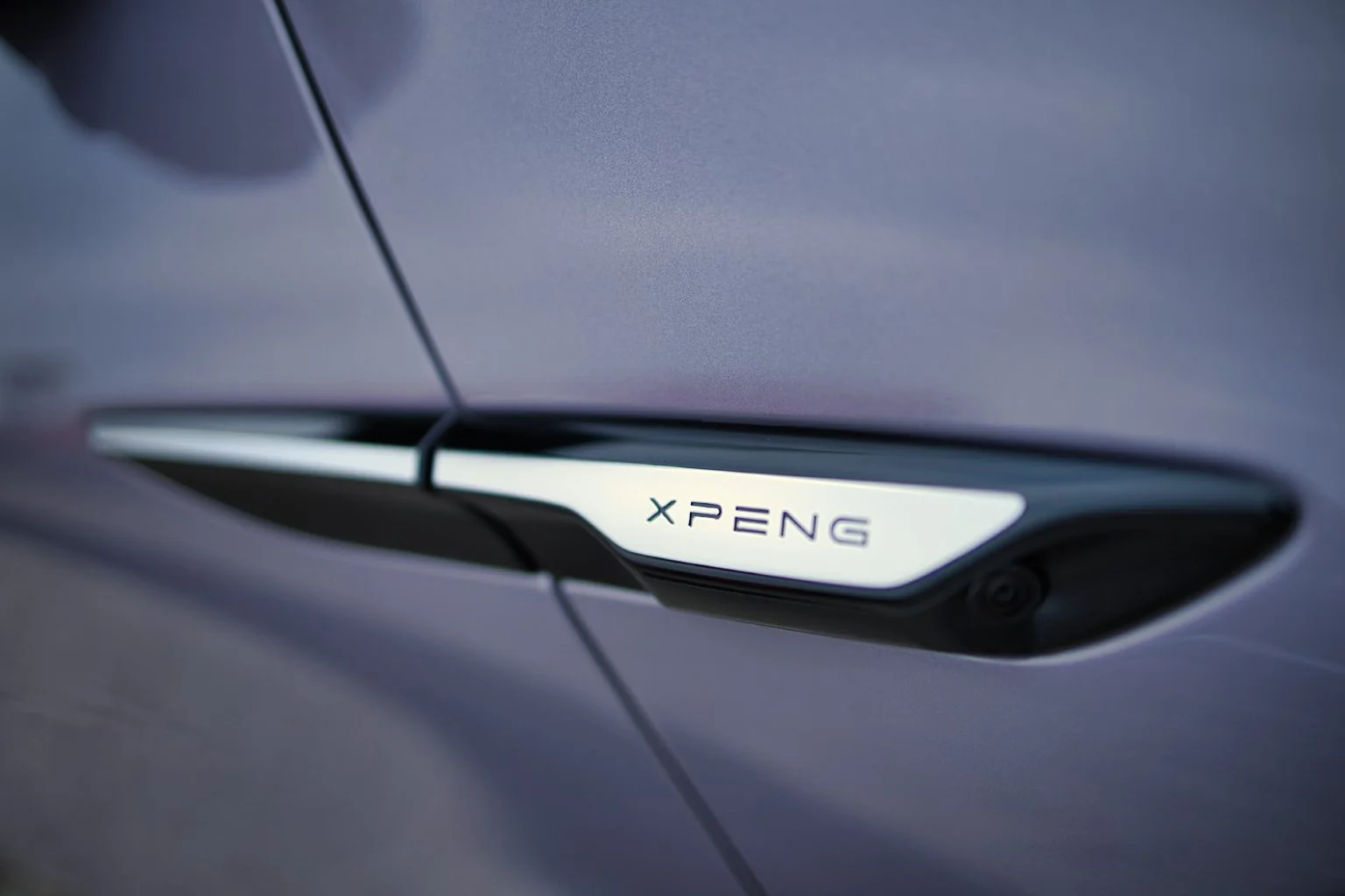 Détail d'une porte de voiture avec une plaque portant l'inscription 'XPENG'.