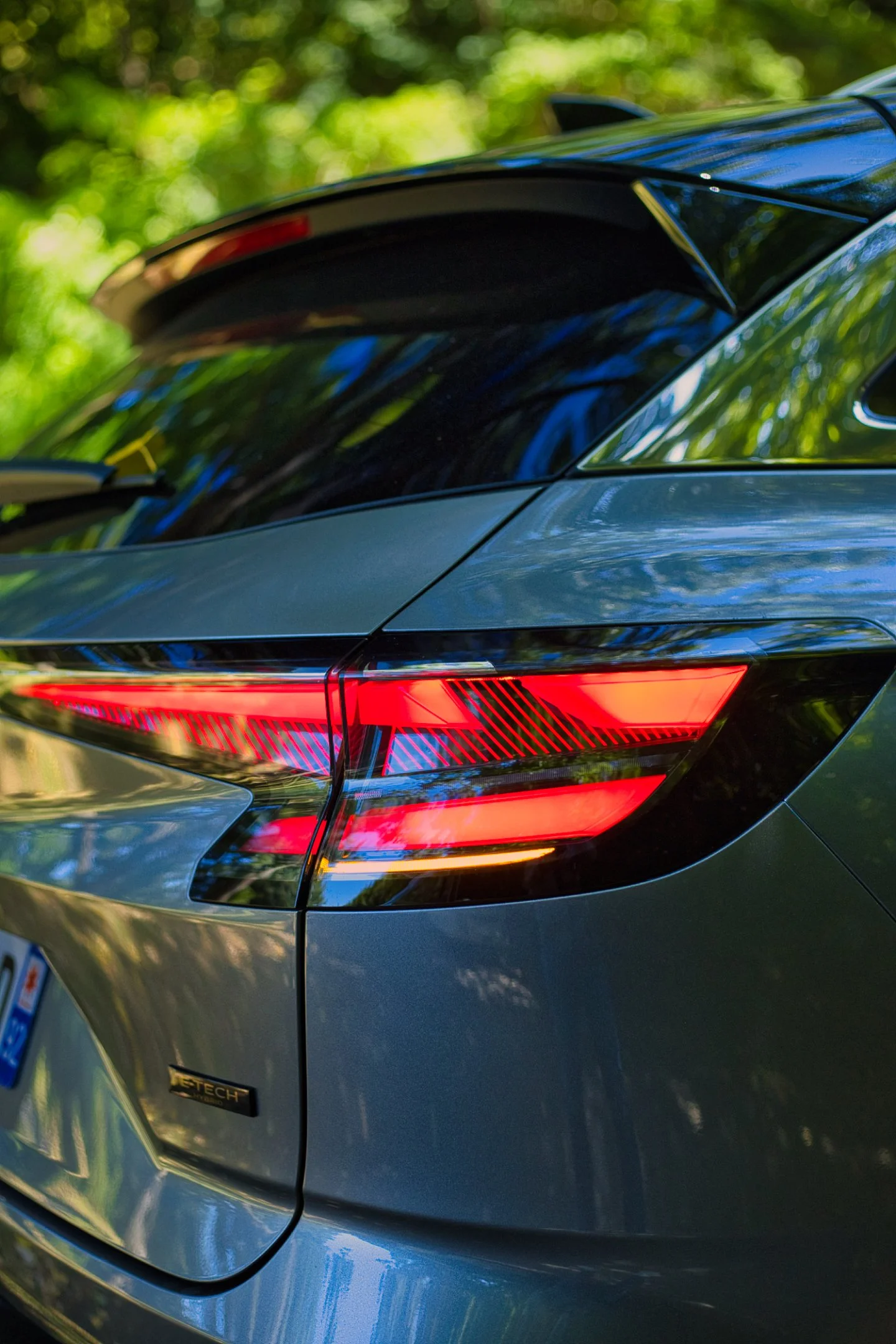 Vue de l'arrière d'une voiture noire avec feux arrière rouges lumineux, dans un environnement boisé. Renault Austral e-tech 200