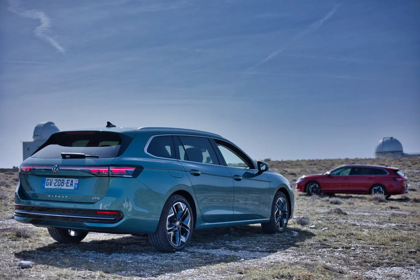 Volkswagen Passat, une bleue et une rouge, stationnées dans un paysage désertique avec des observatoires astronomiques en arrière-plan sous un ciel clair.