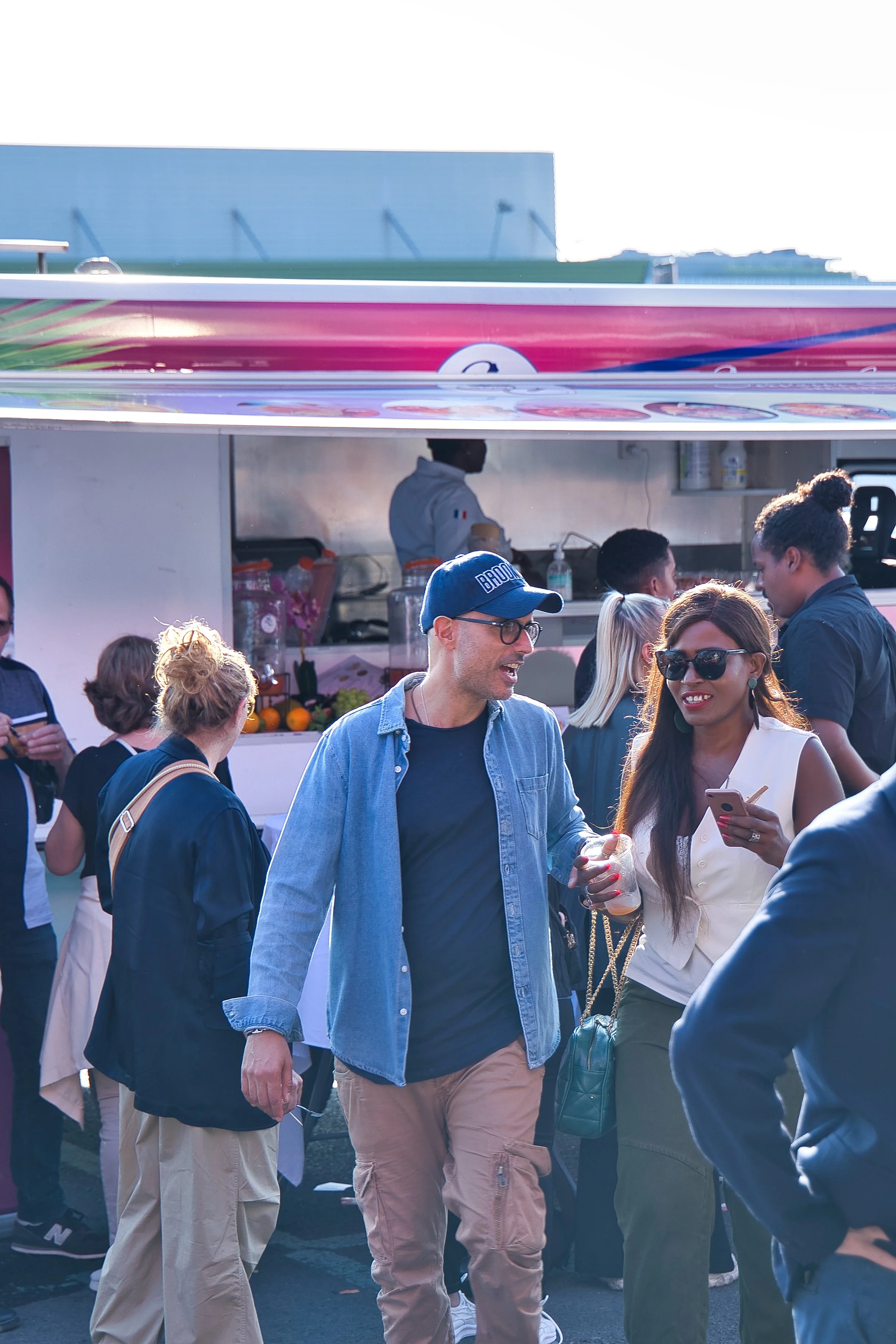 Groupe de personnes conversant devant un stand de nourriture ou de boissons en extérieur.