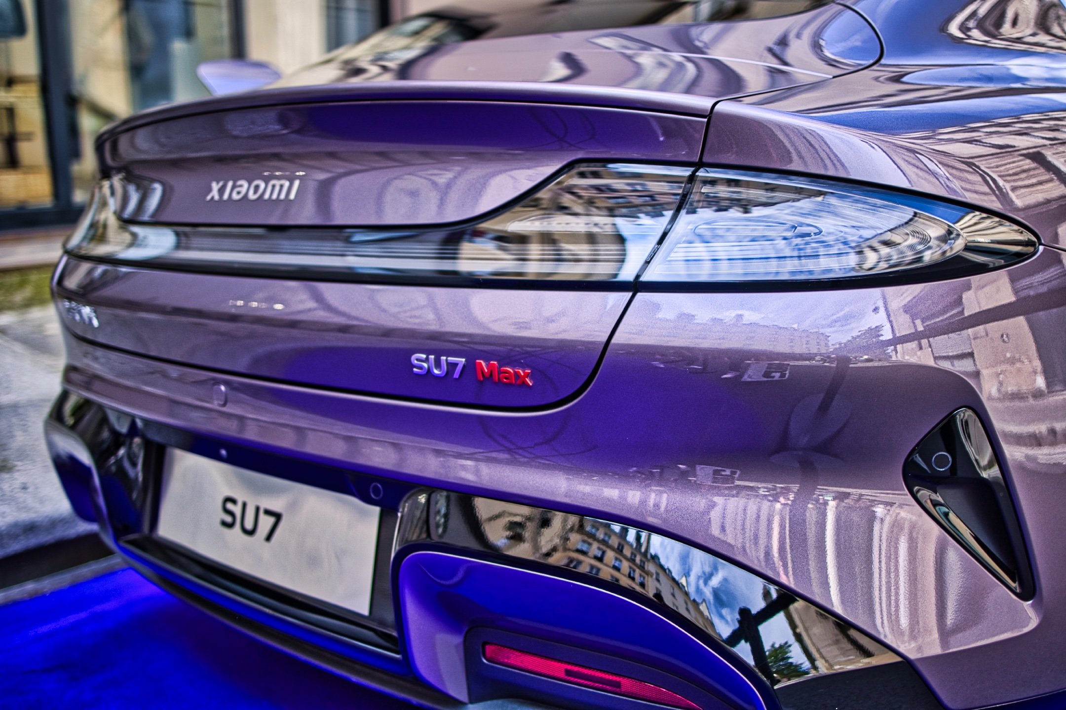 Vue arrière d'une voiture violette SU7 Max, with reflections of buildings on its surface. Xiaomi SU7 Max