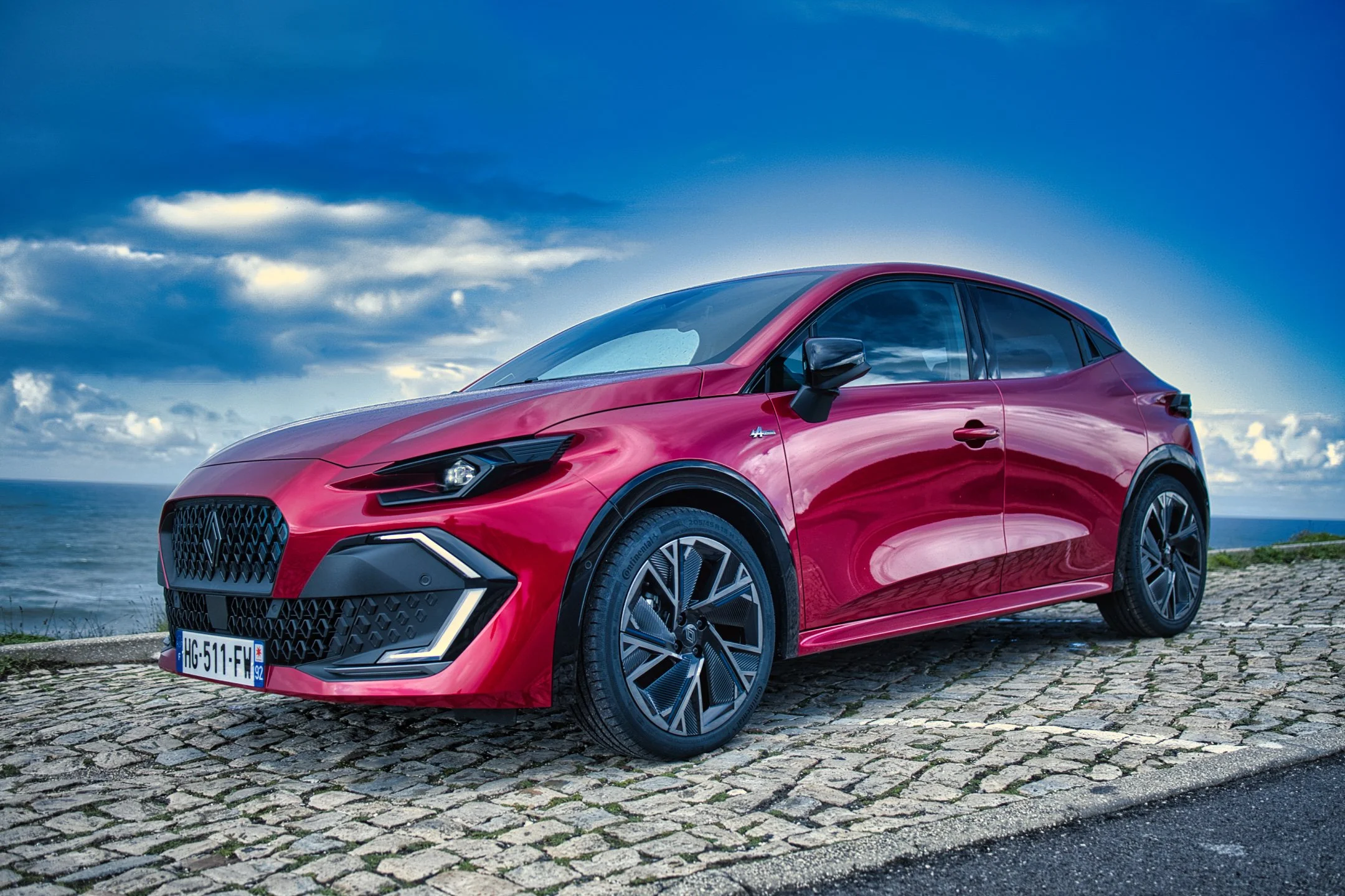 Nouvelle Renault Clio VI stationnée sur une voie pavée près de la mer, avec un ciel nuageux en arrière-plan.