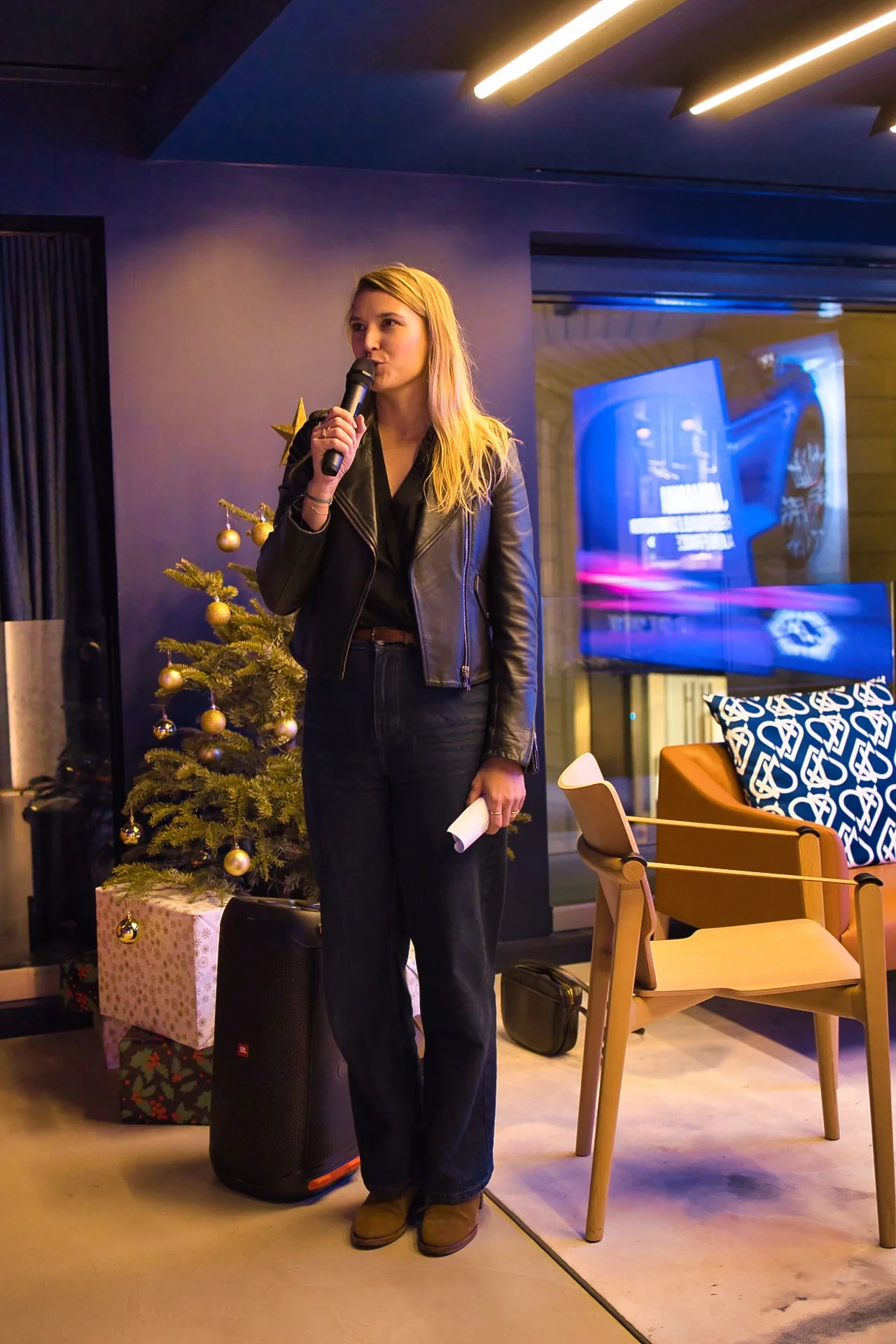 Une femme avec des cheveux blonds portant une veste en cuir noire parle dans un micro, à l'atelier Alpine à Paris