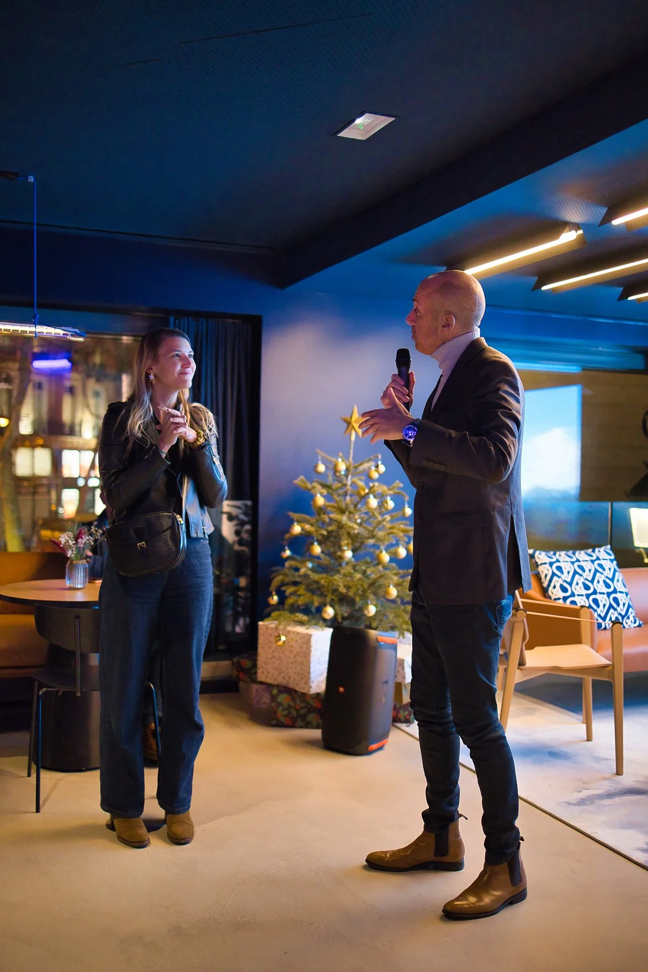 Un homme et une femme discutent dans une pièce décorée pour Noël, avec un sapin de Noël en arrière-plan.
