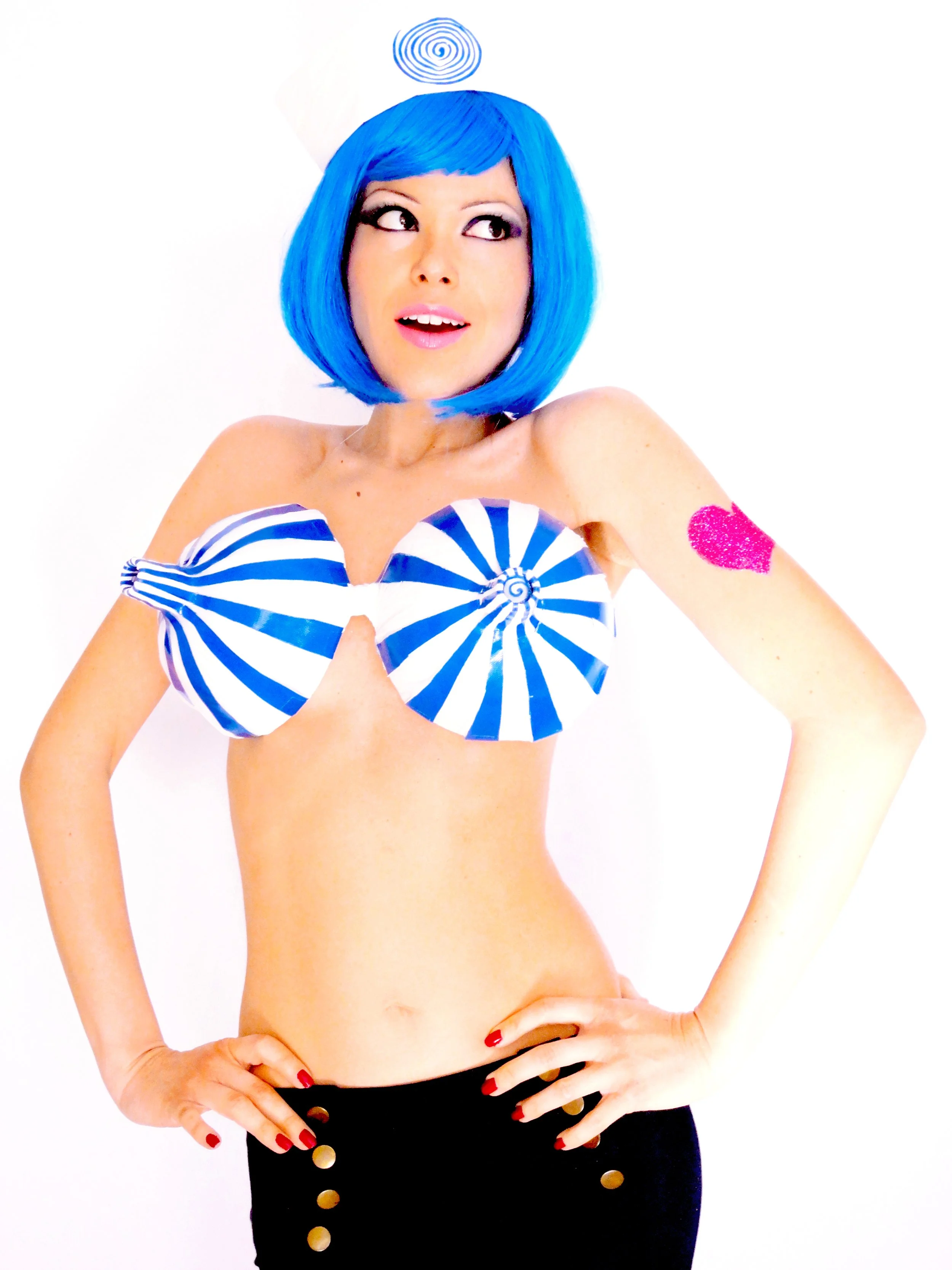 Woman with blue wig and blue-and-white striped top, winking, standing with hands on hips
