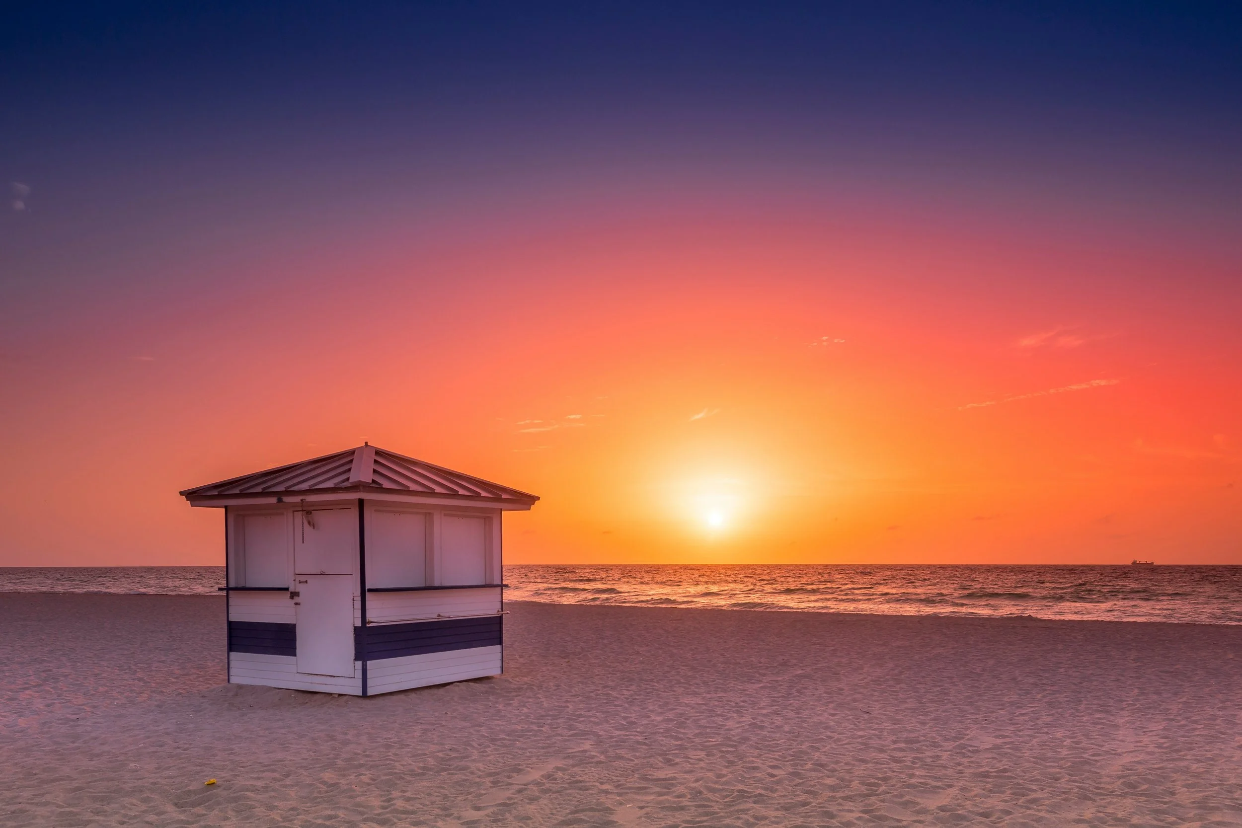 Grove Key Collective vero beach Sunset over the ocean with a colorful sky, a small white beach hut on the sand in the foreground.
