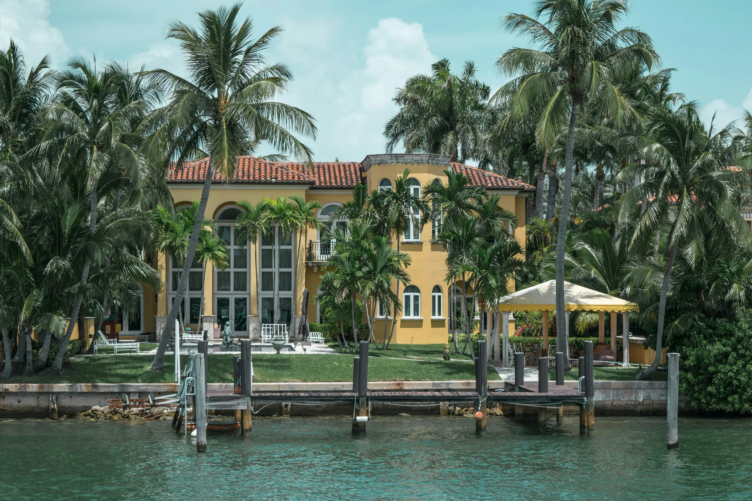 A yellow mansion by the water with palm trees, a small dock, and a gazebo Vero Beach