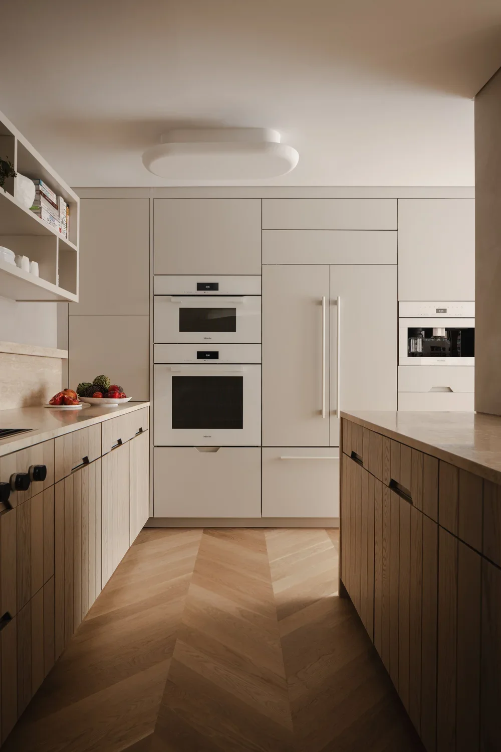 Modern kitchen with light-colored cabinetry, built-in stainless steel appliances, wooden lower cabinets, and a wooden floor arranged in a herringbone pattern.