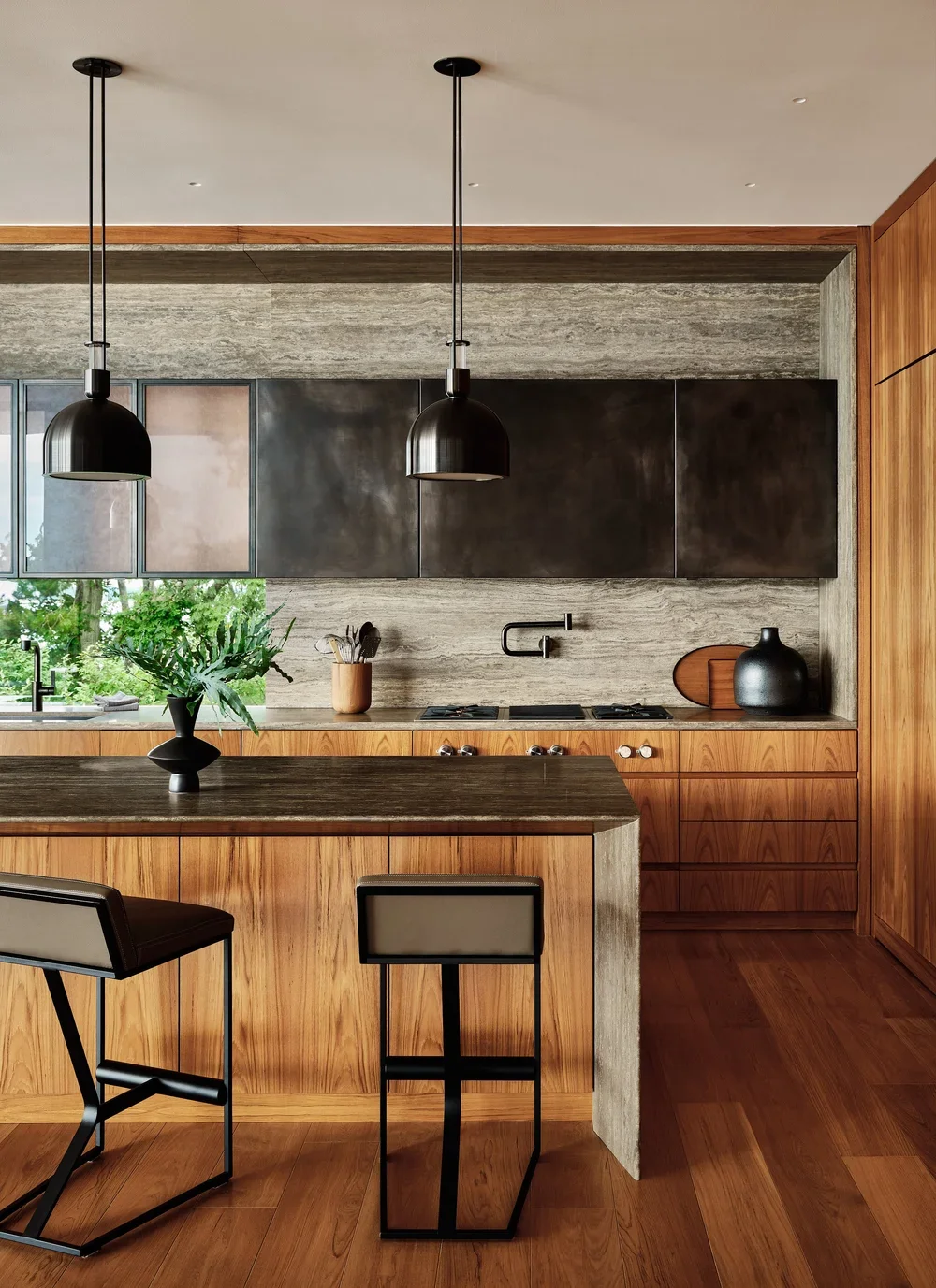 Modern kitchen with black pendant lights, wooden cabinets, gray textured wall, black appliances, and a kitchen island with two black and white stools.
