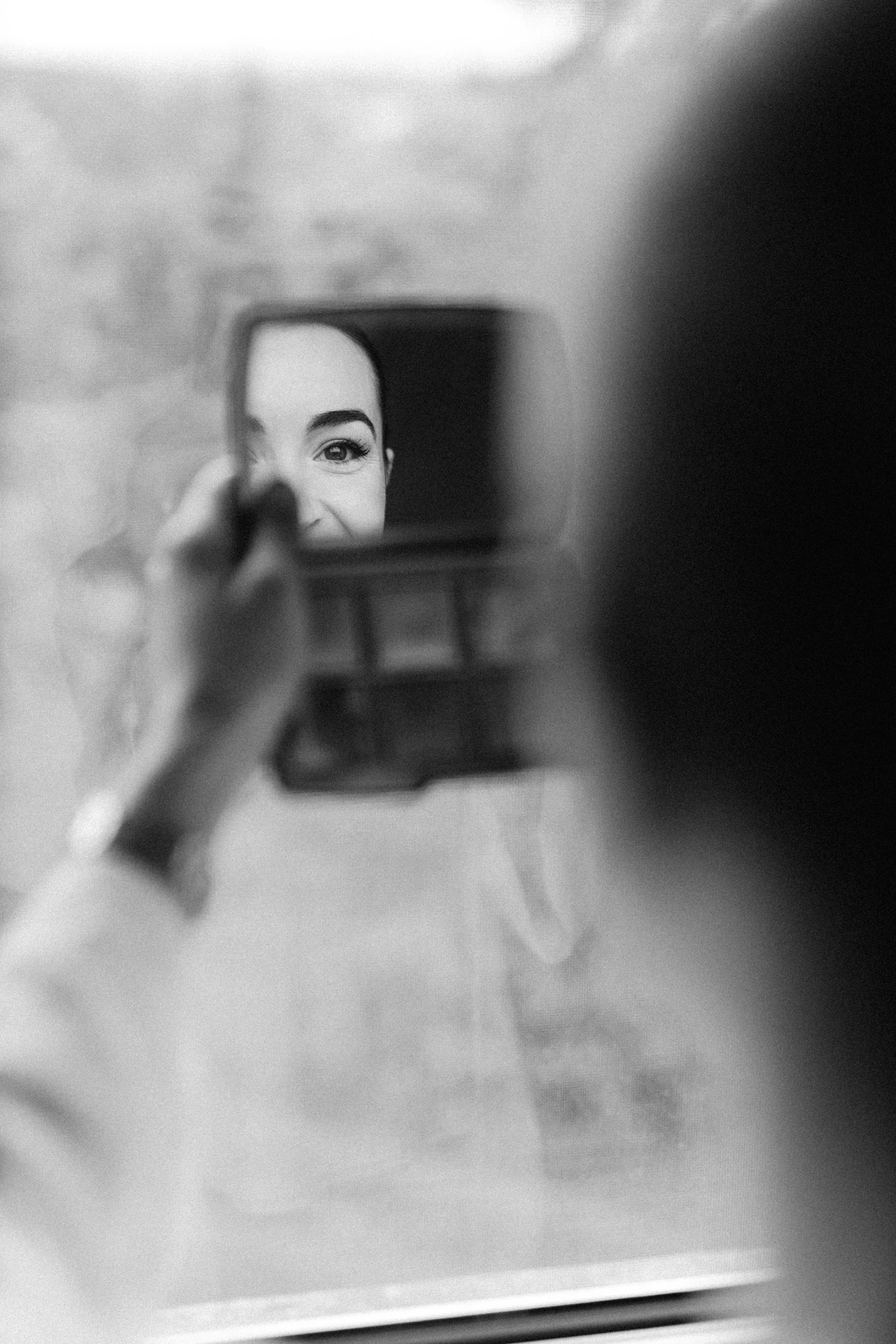 Black and white photo of a woman taking a selfie in a mirror, showing part of her face including eyes, eyebrows, and forehead.