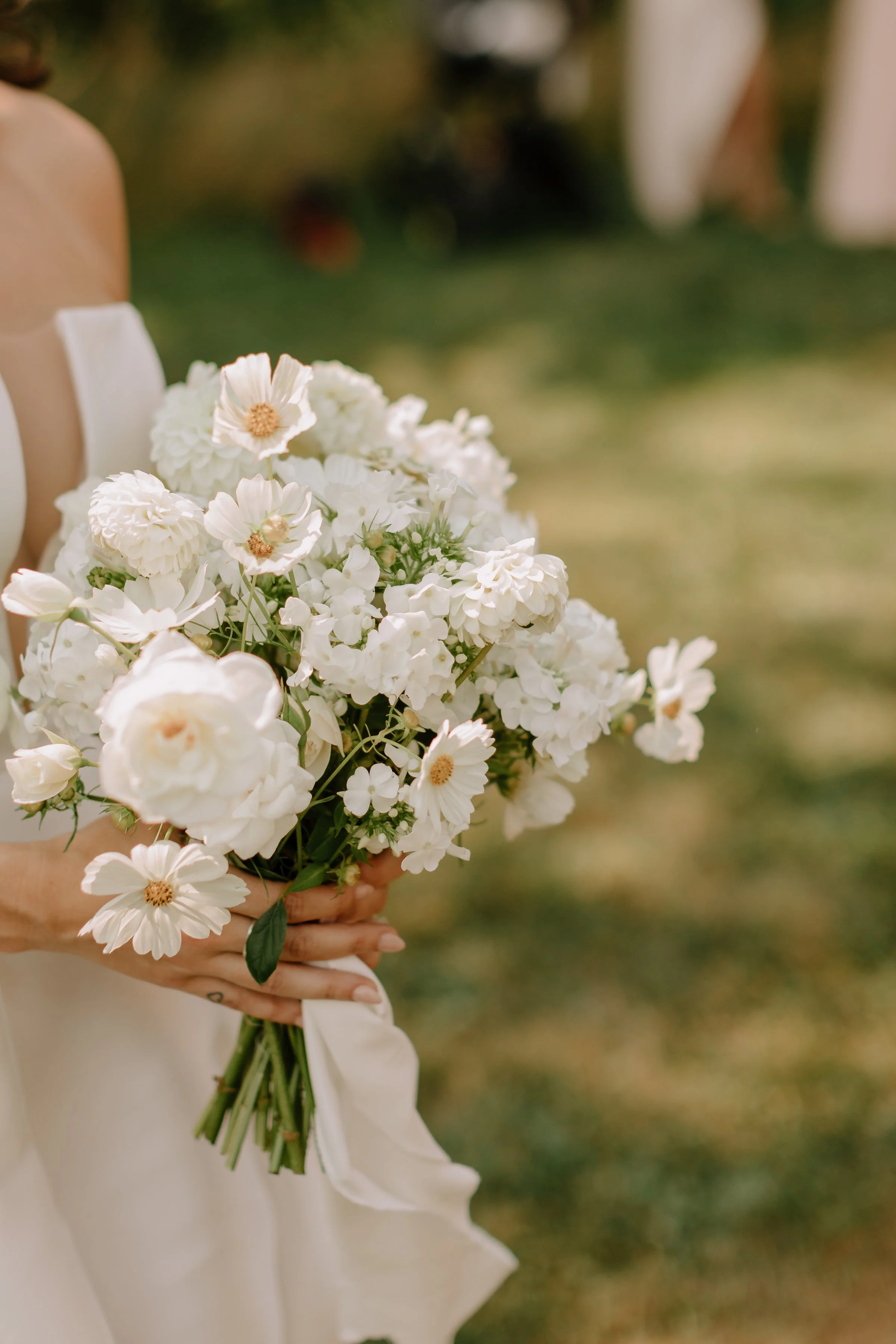 A person holding a bouquet of white and cream flowers outdoors.