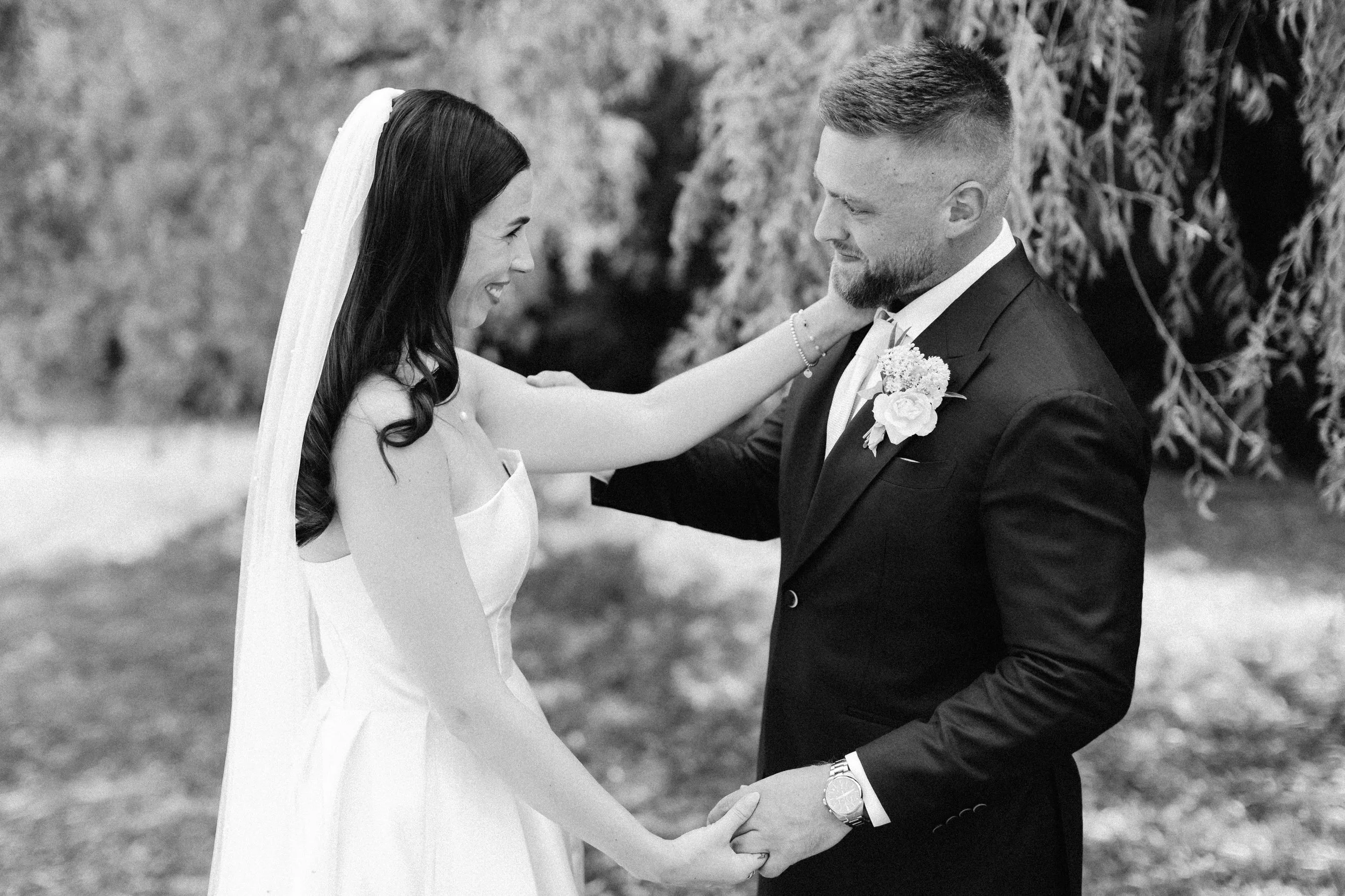 A bride and groom holding hands during their wedding ceremony outdoors, smiling at each other.