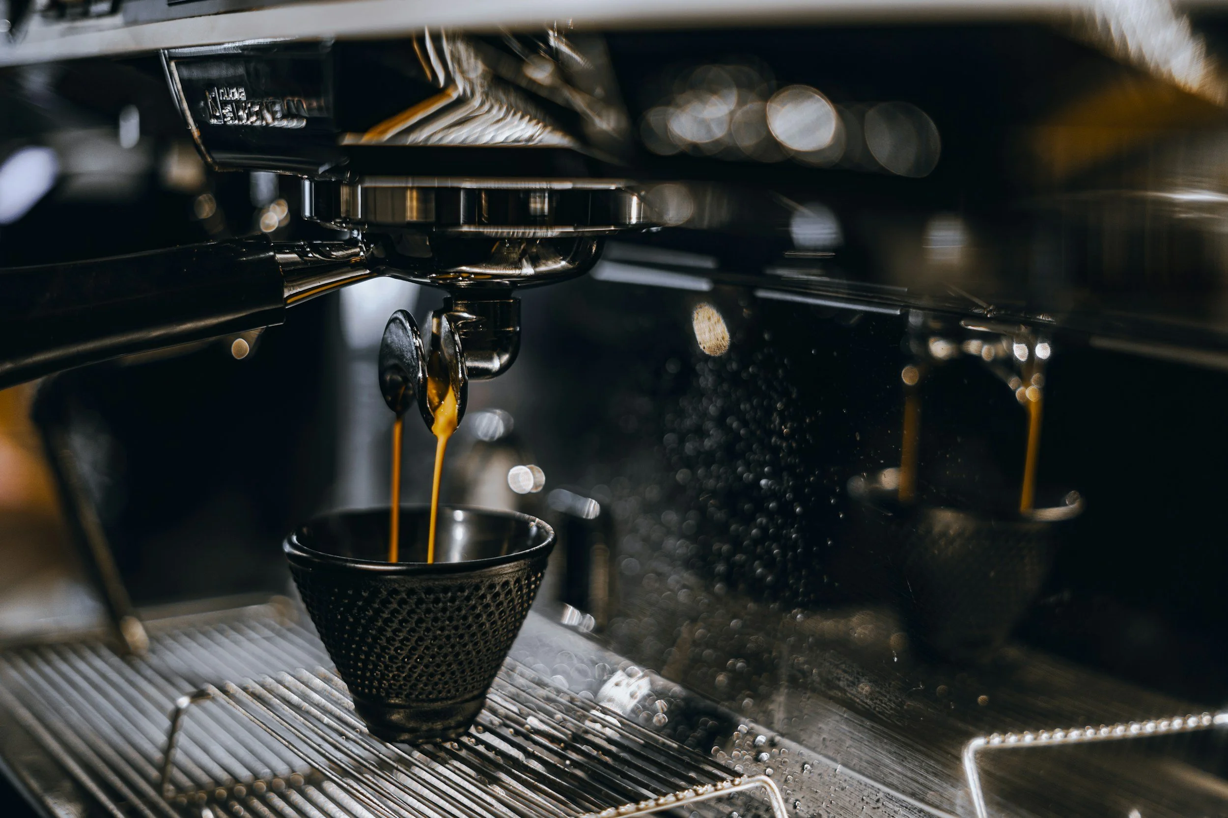 Close-up of an espresso machine dispensing coffee into a small cup, with steam and liquid visible.