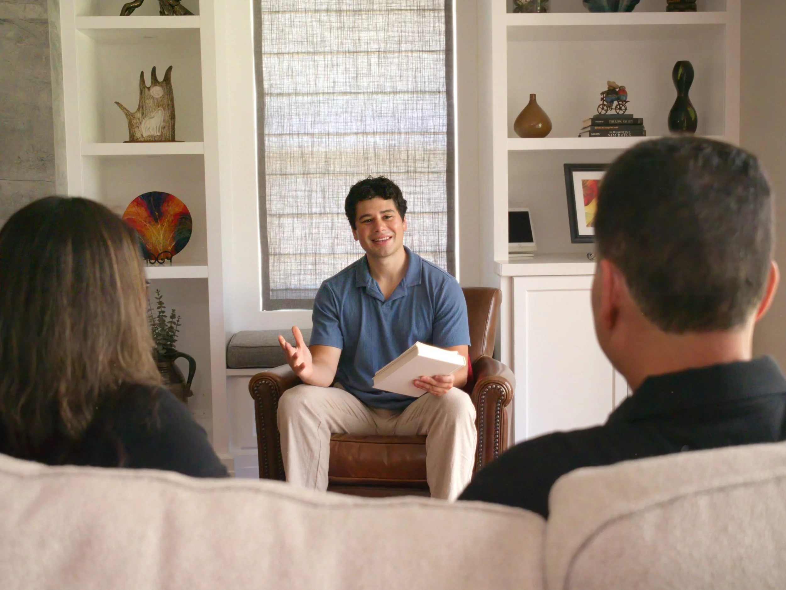 Luis Lopez speaking with a small group in a room with bookshelves.