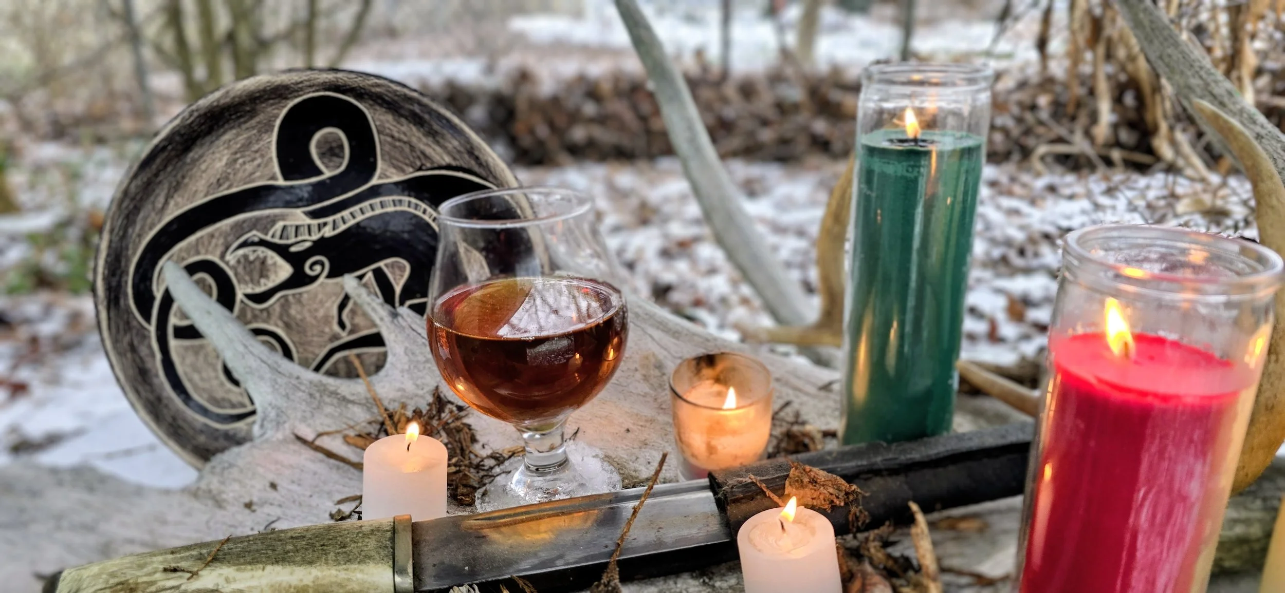 Glass of amber colored mead on an outside altar with candles, a bone handled knife and a Norse dragon designed altar plate