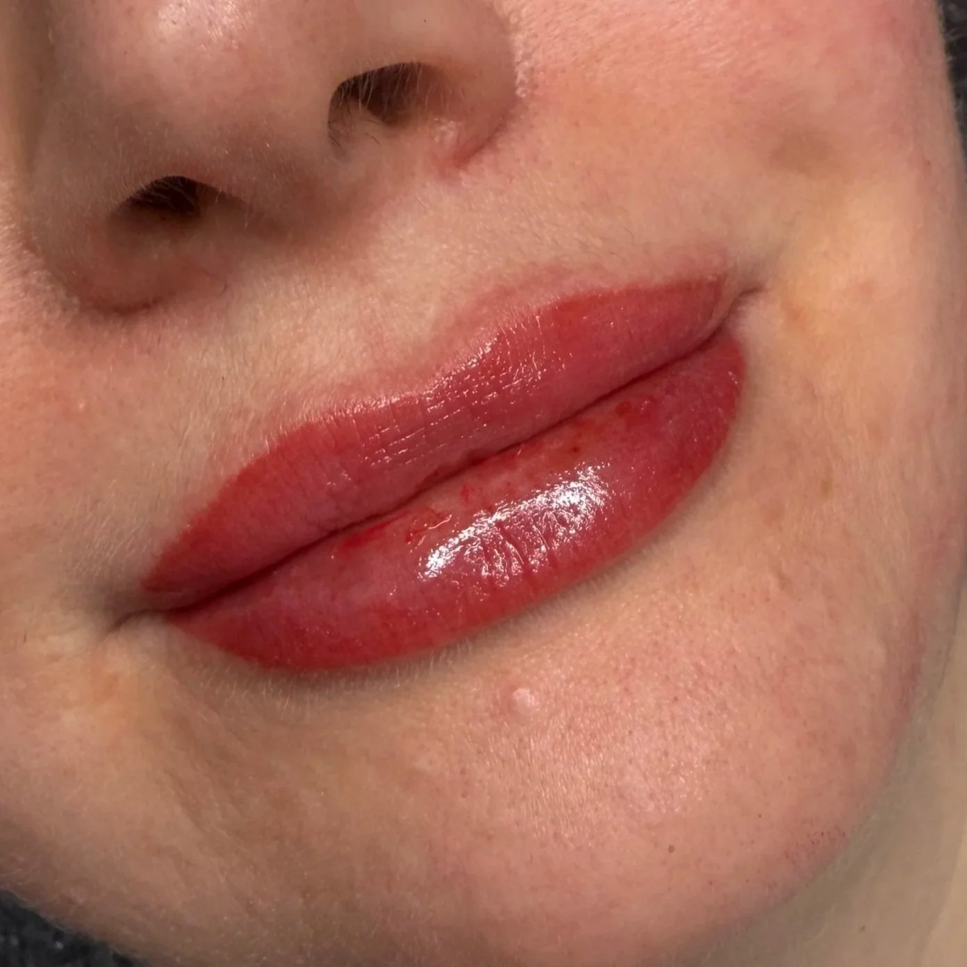Close-up of a person's lips with glossy lip gloss and a natural skin texture around the mouth.