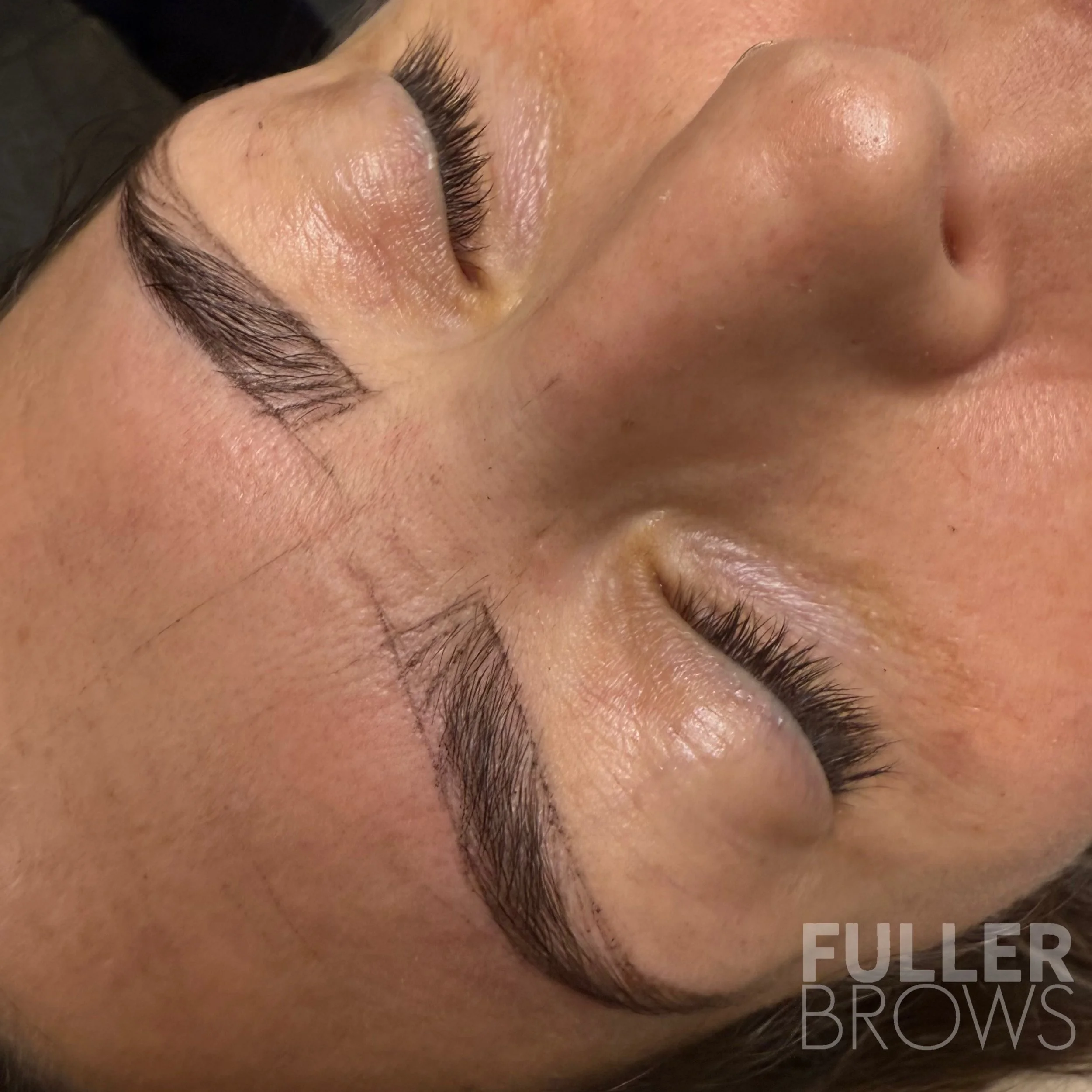 Close-up of a woman's face with freshly microbladed eyebrows, manicured with sharp, dark strokes for a natural look, and smooth skin.
