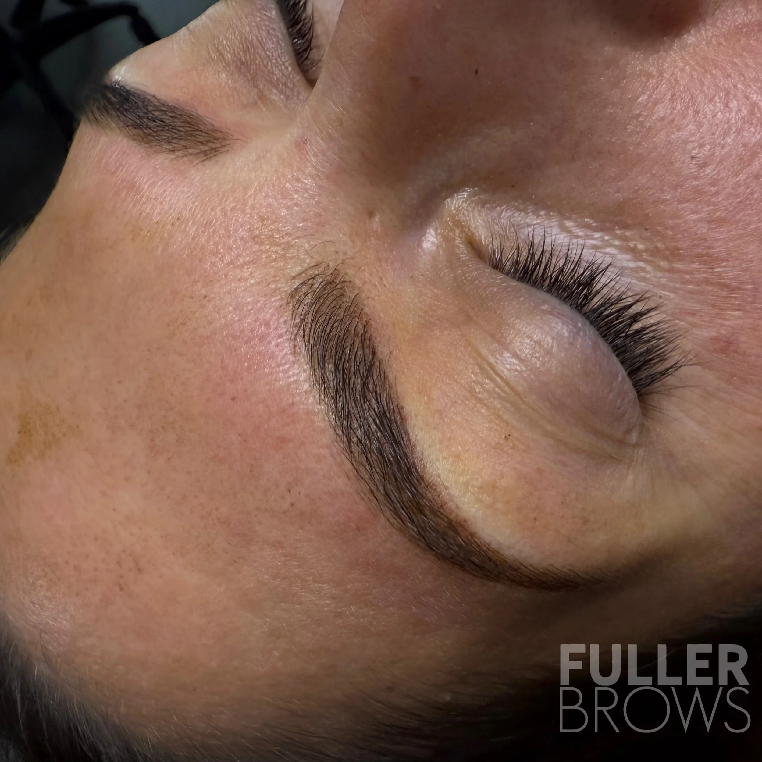 Close-up of a person's face showing freshly groomed, dark, thick eyebrows and closed eyes with long curled eyelashes. Skin appears smooth with natural texture.