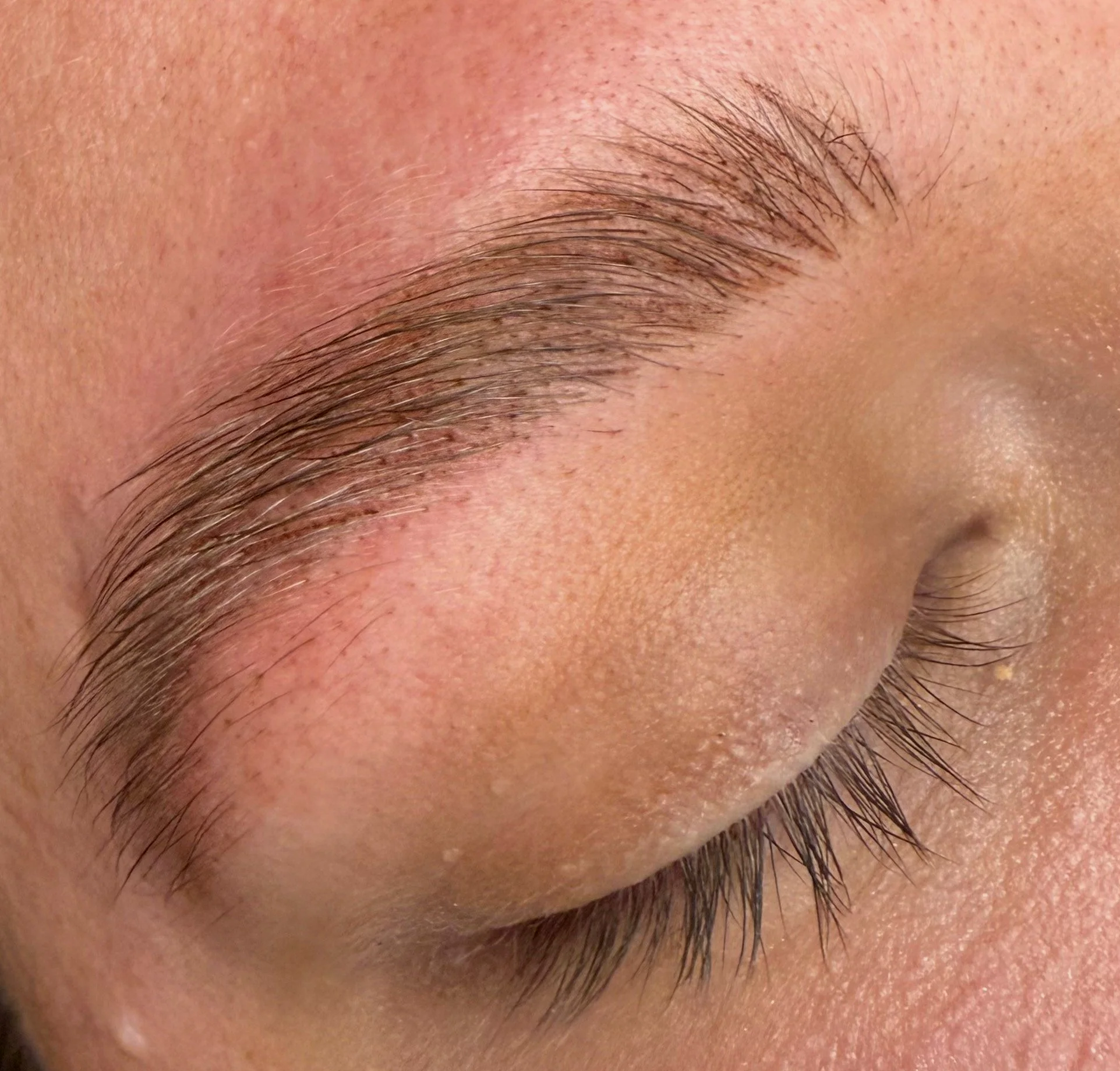Close-up of a person's closed eye, showing detailed eyelash and eyebrow hair, with smooth skin and some fine skin texture.