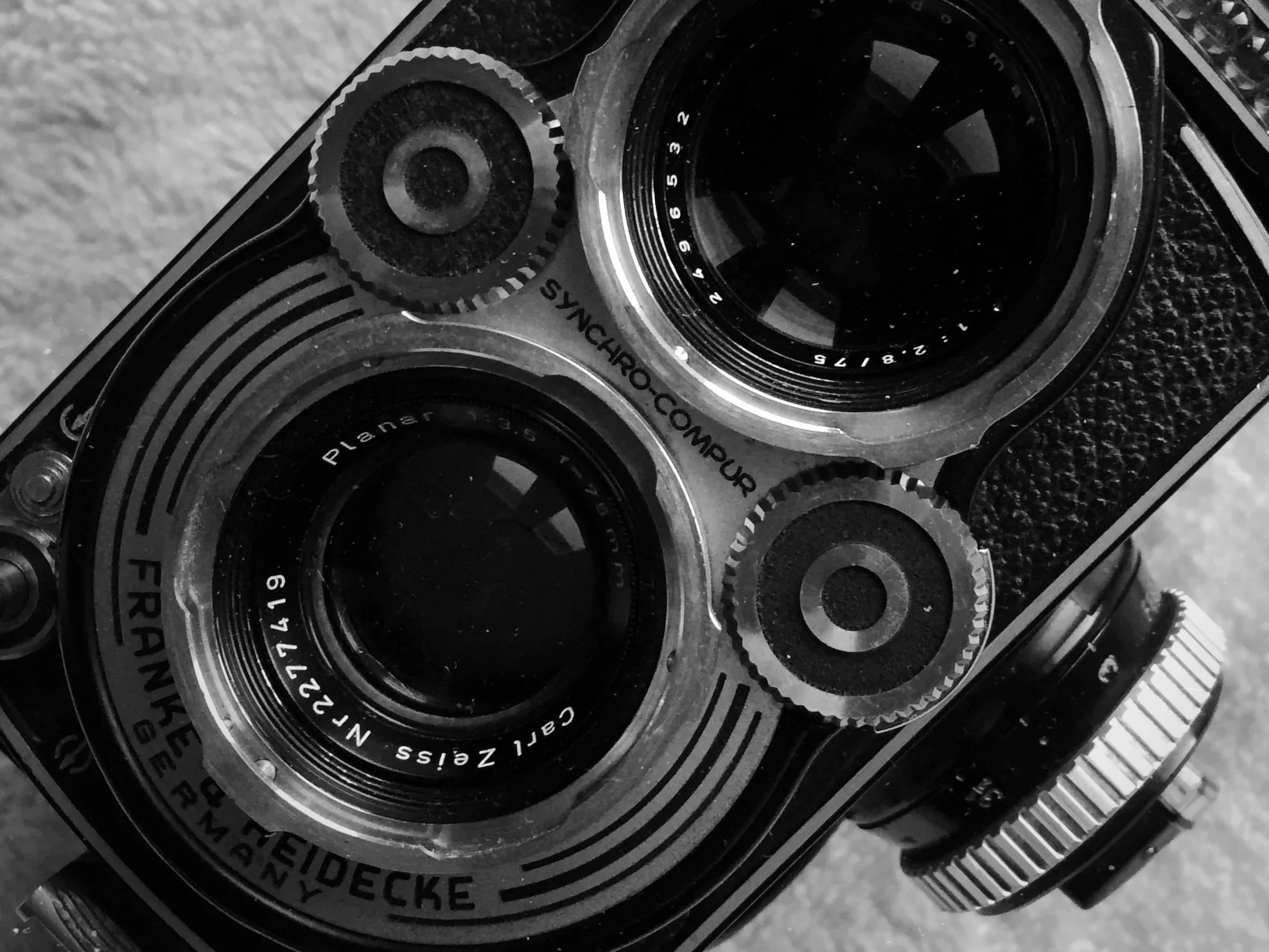 Close-up black-and-white photo of a vintage camera, focusing on the camera's lens and dials with detailed markings.