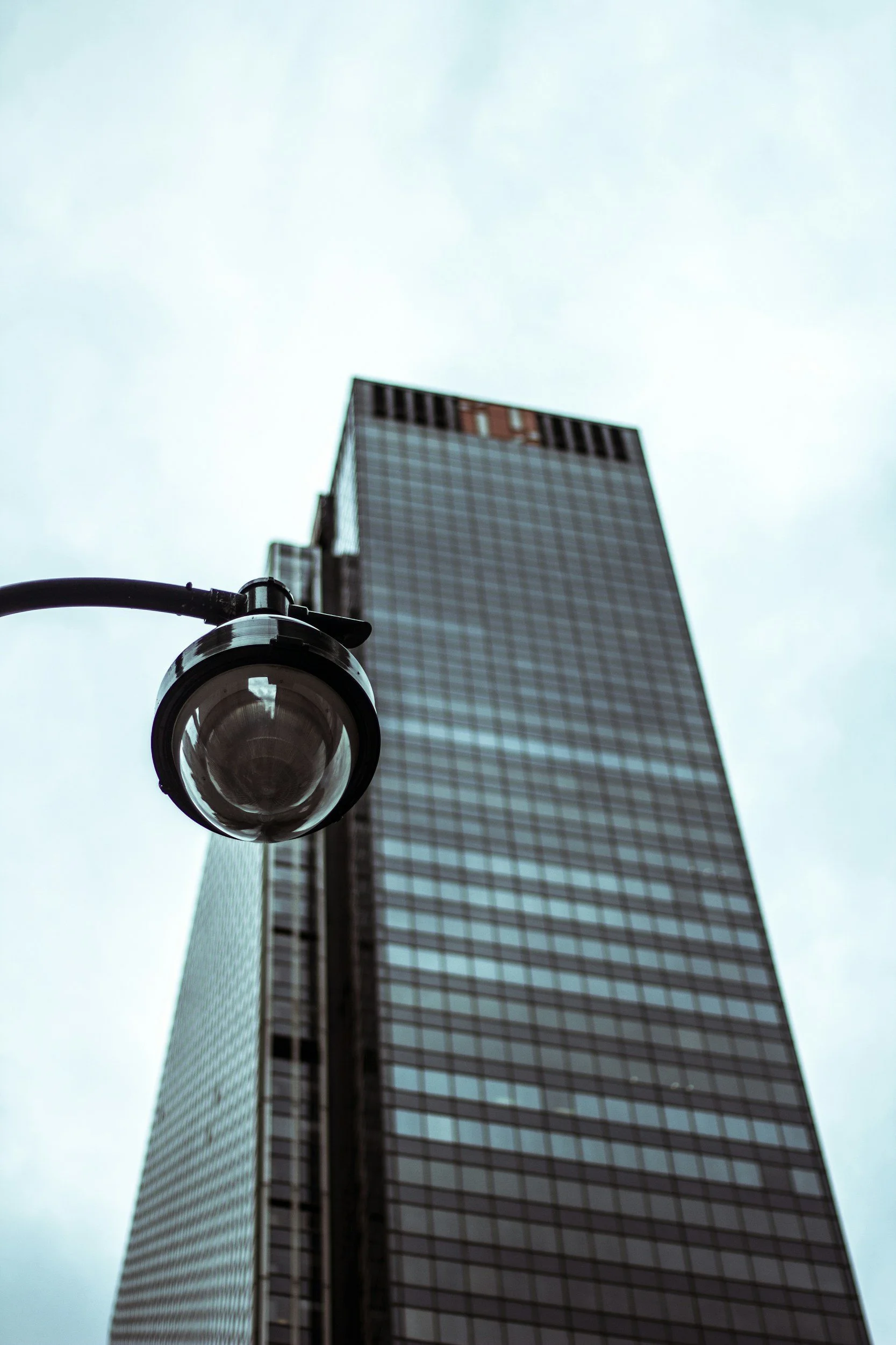 Low angle view of a streetlamp in front of a tall modern glass skyscraper on a cloudy day.