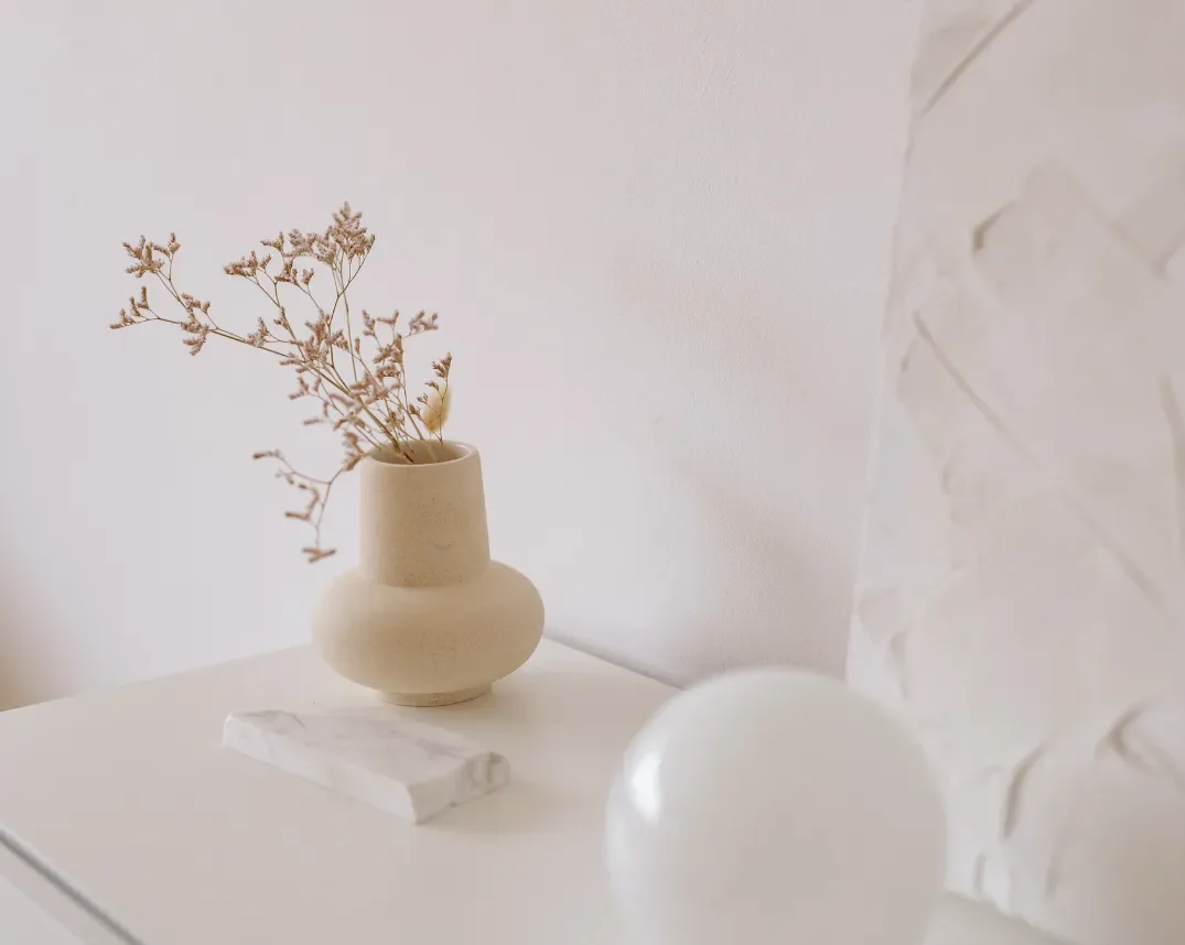 Minimalist scene with a beige vase holding dried flowers on a white surface.