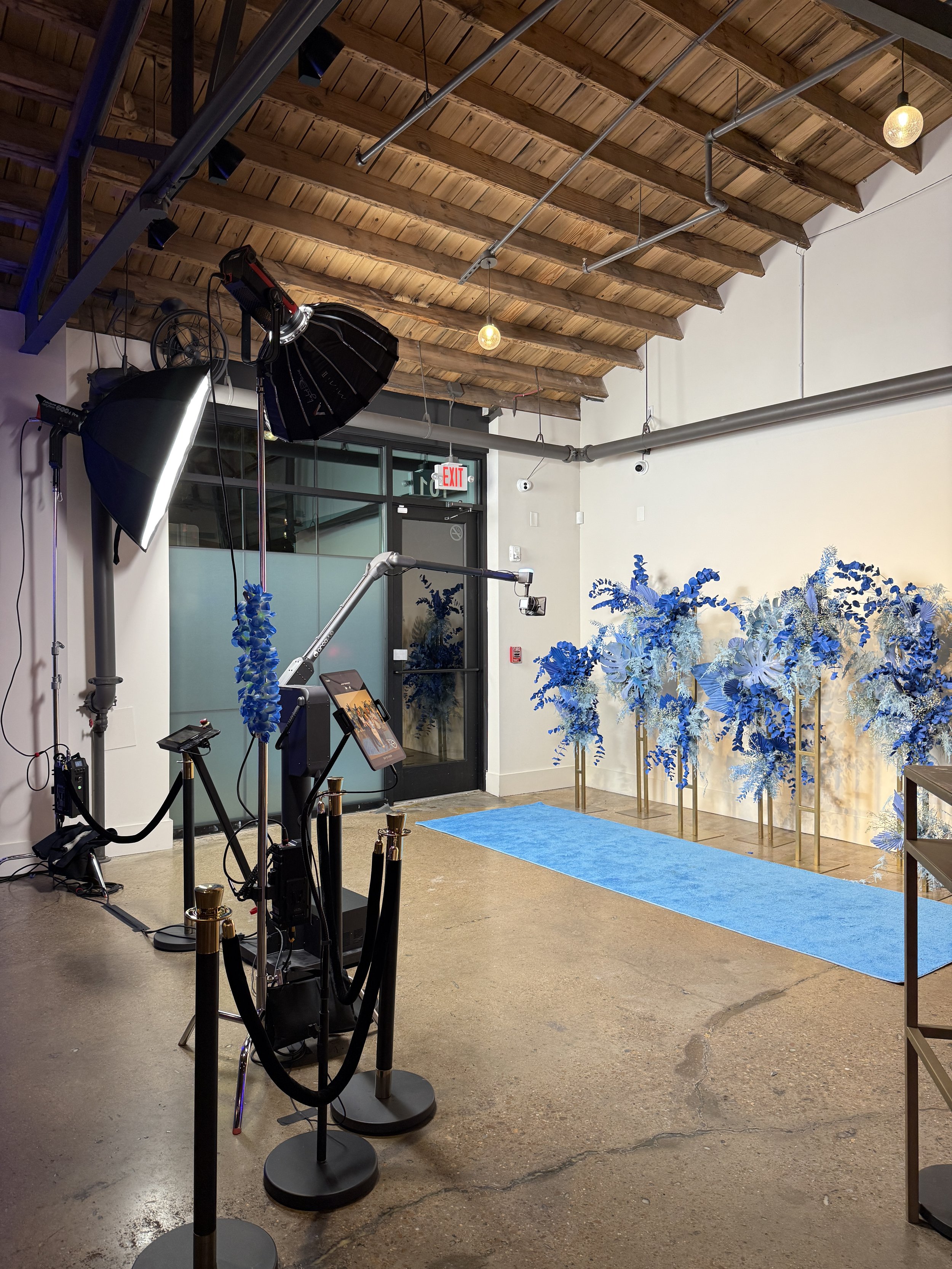 Photography setup with a glambot with blue floral backdrop, overhead wooden ceiling, and professional lighting equipment