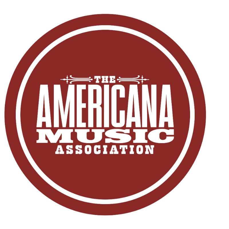 A circular emblem with a red background and black border. Inside, it reads "The Americana Music Association" with "Americana" in large bold letters.