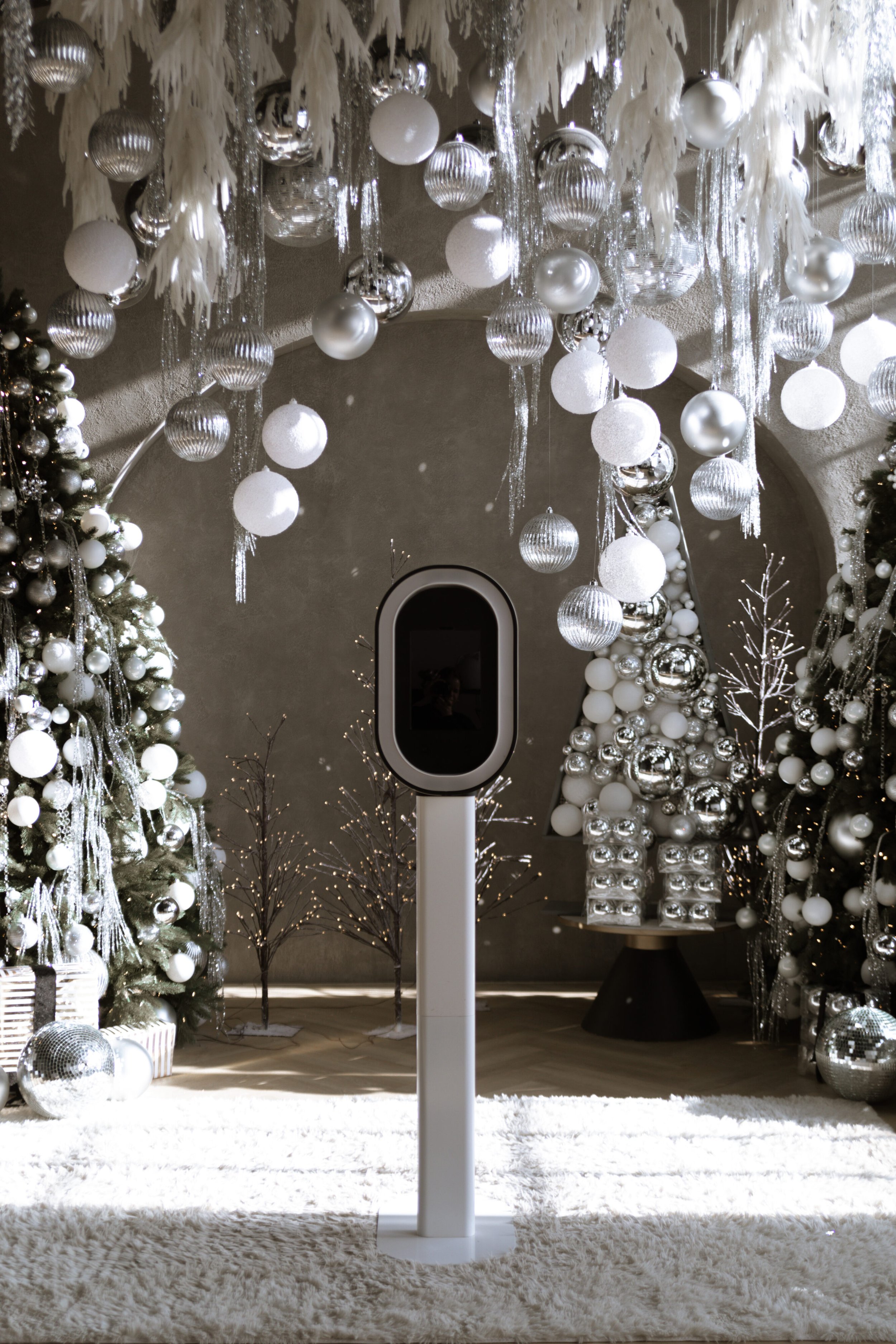 A display with white and silver Christmas trees, ornaments, and hanging decorations, with a robot in the center.