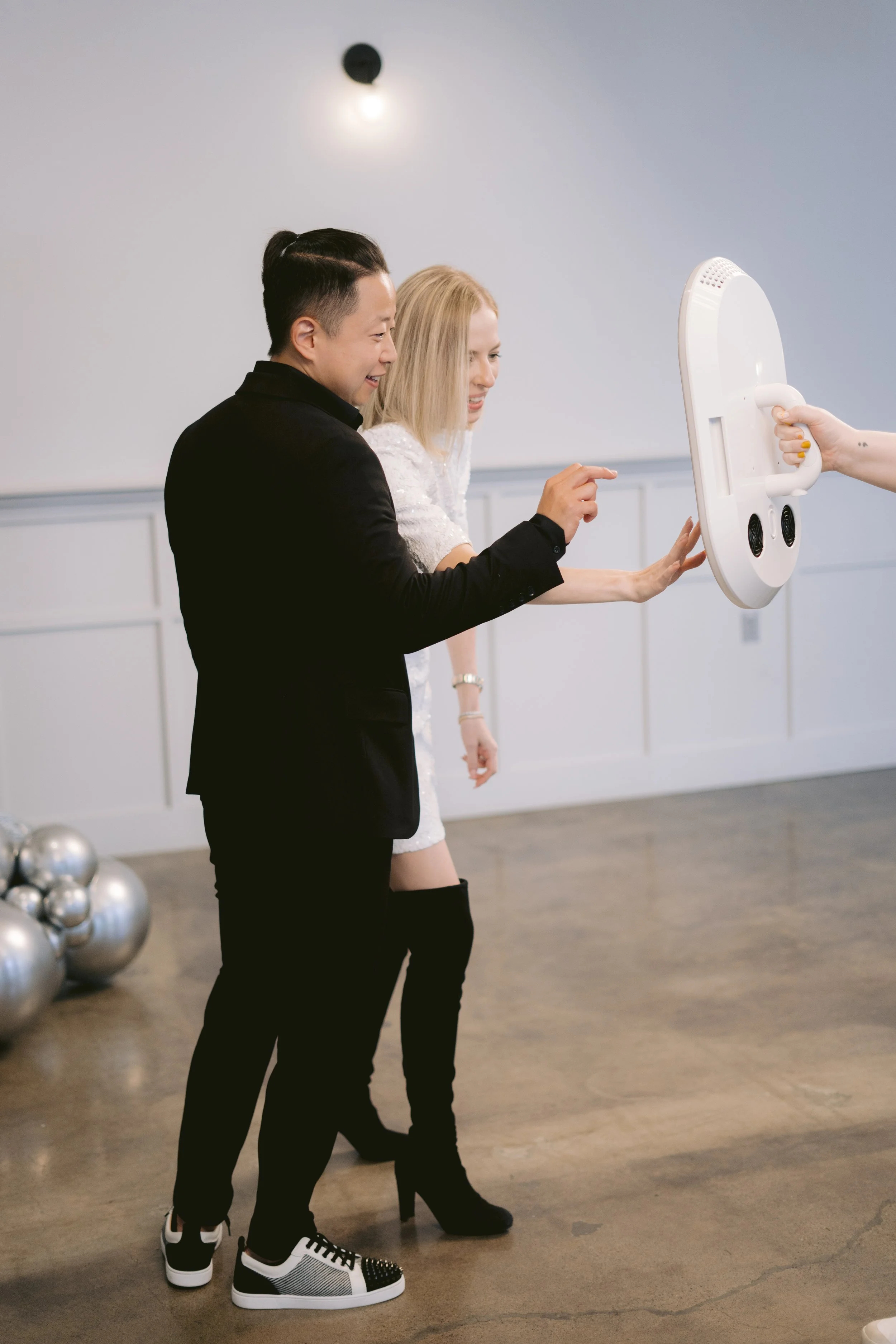 Two women and one man smiling and taking a photo with a roaming photo booth, indoors with a concrete floor and metallic decorations in the background.