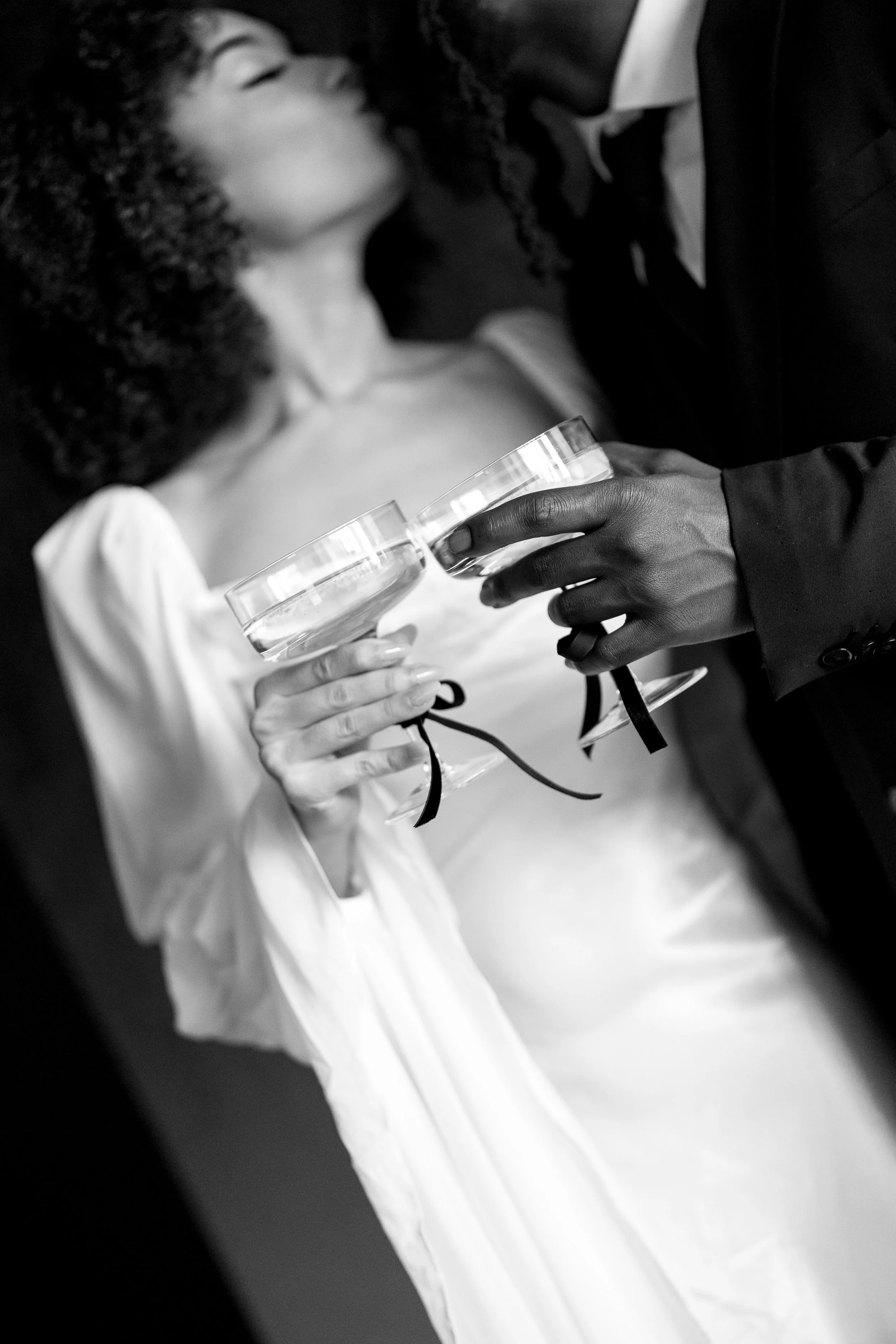 Black and white photo of a bride and groom holding glasses of champagne during their wedding celebration.
