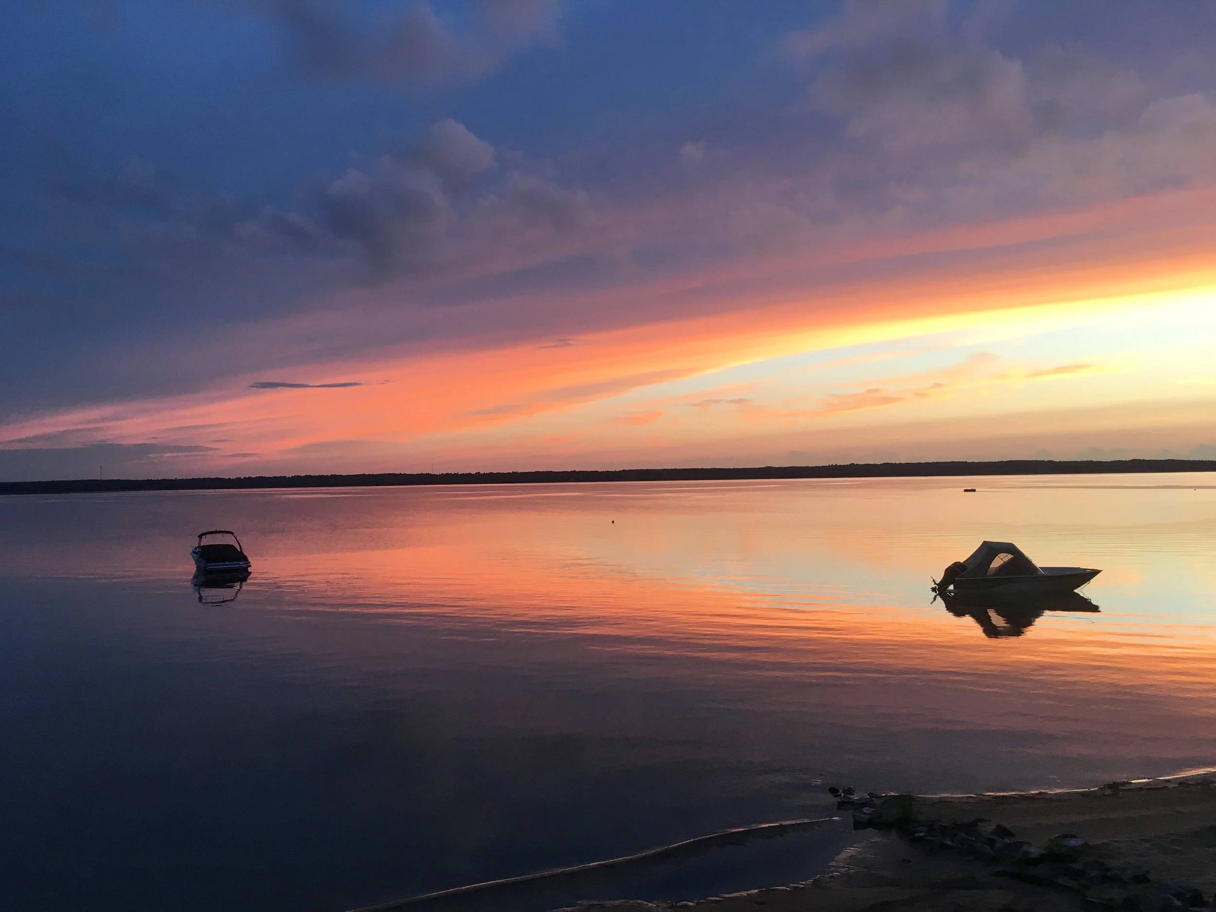 Two boats resting apart on the same lake under a pink and blue evening sky.
