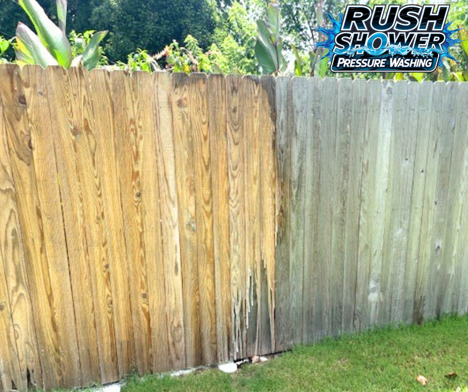 A wooden backyard fence with one side weathered and discolored, next to a new section. There is grass at the base of the fence and some plants at the top. The top right corner has a logo for 'Rush Shower Pressure Washing'.