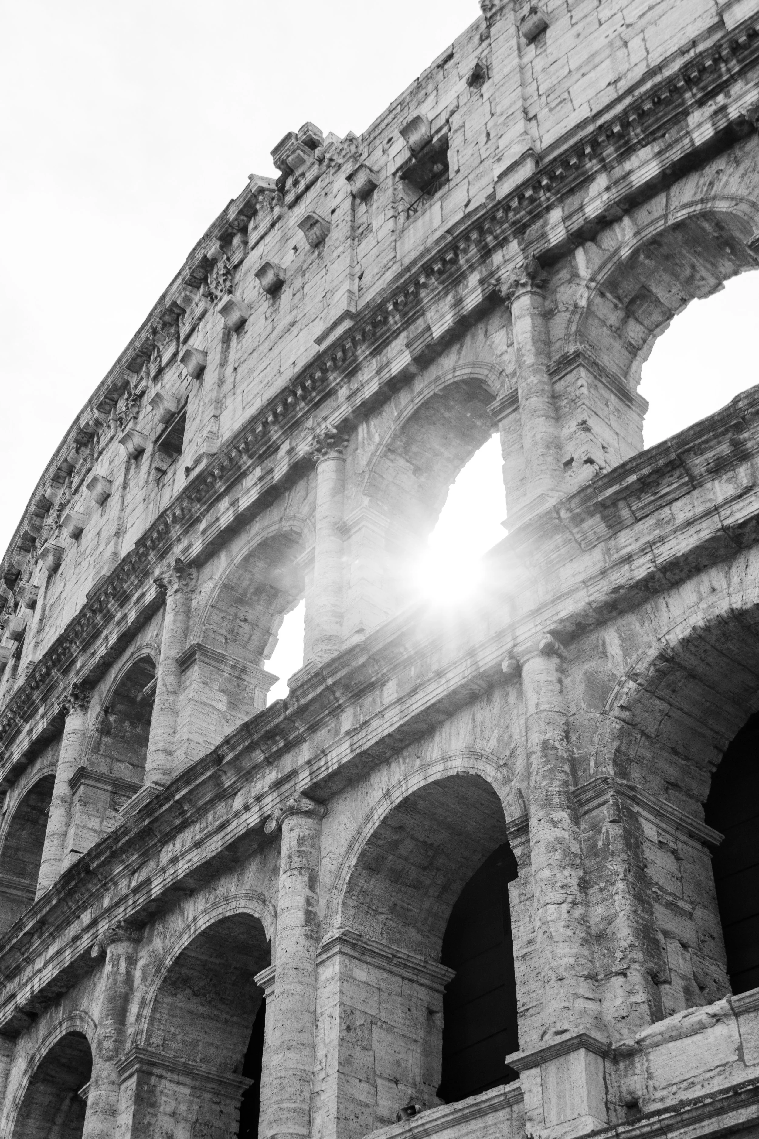 Black and white photo of the Leaning Tower of Rome with sunlight shining through an arch.