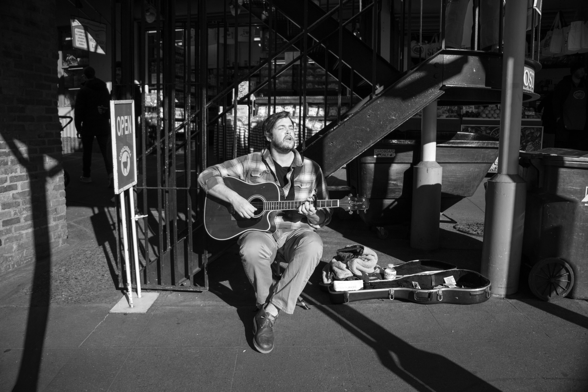 A man sitting on the sidewalk playing an acoustic guitar with his eyes closed.