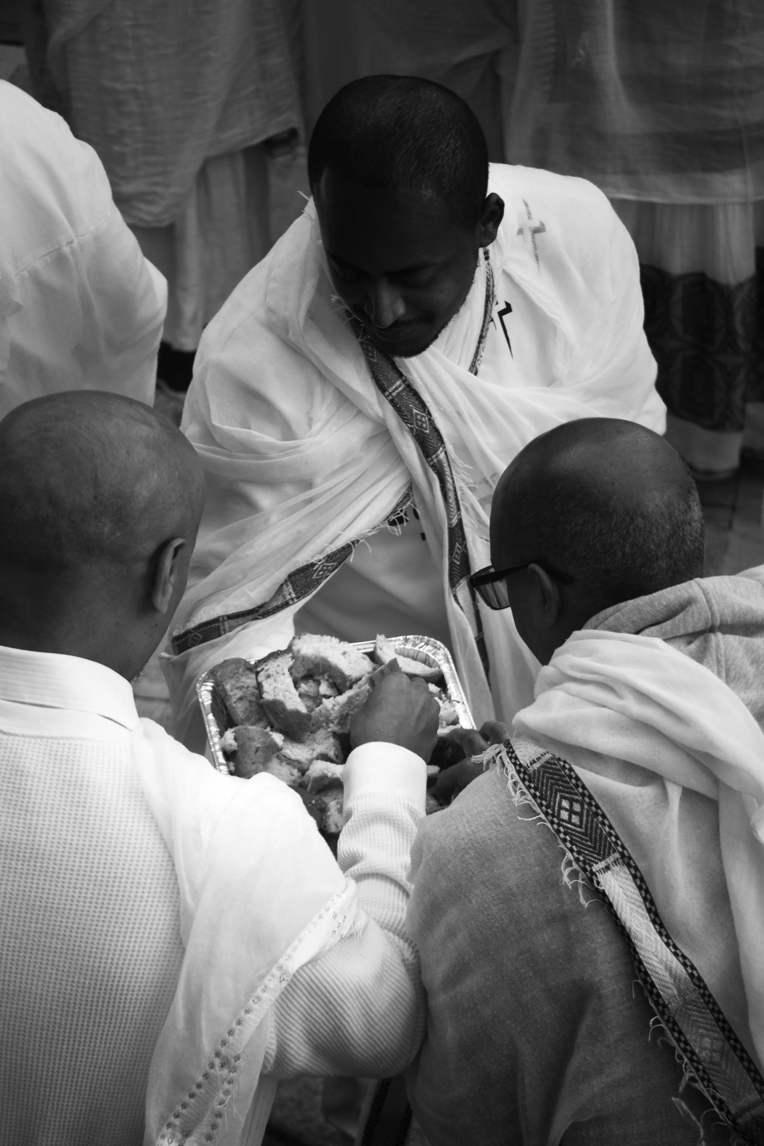 A traditional Ethiopian religious ceremony with a priest and several men gathered around a tray of bread, possibly sharing a religious or cultural ritual.
